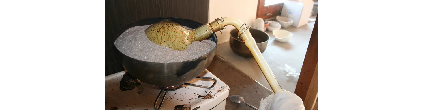 Destillation im Labor. Glaskolben im Sanbad mit gelber Substanz.