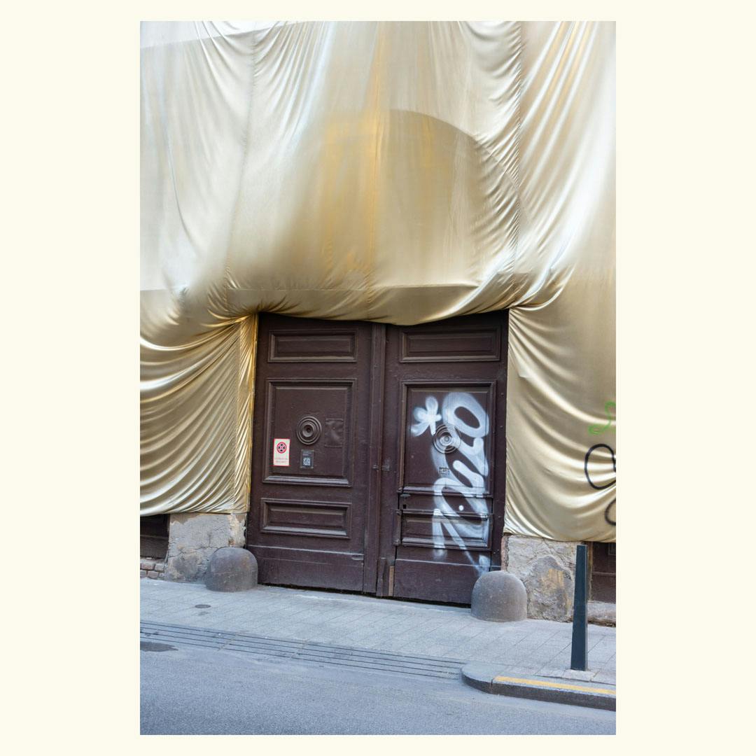 A big brown wooden door with graffiti, above and to the sides a gold-colored fabric covers the facade