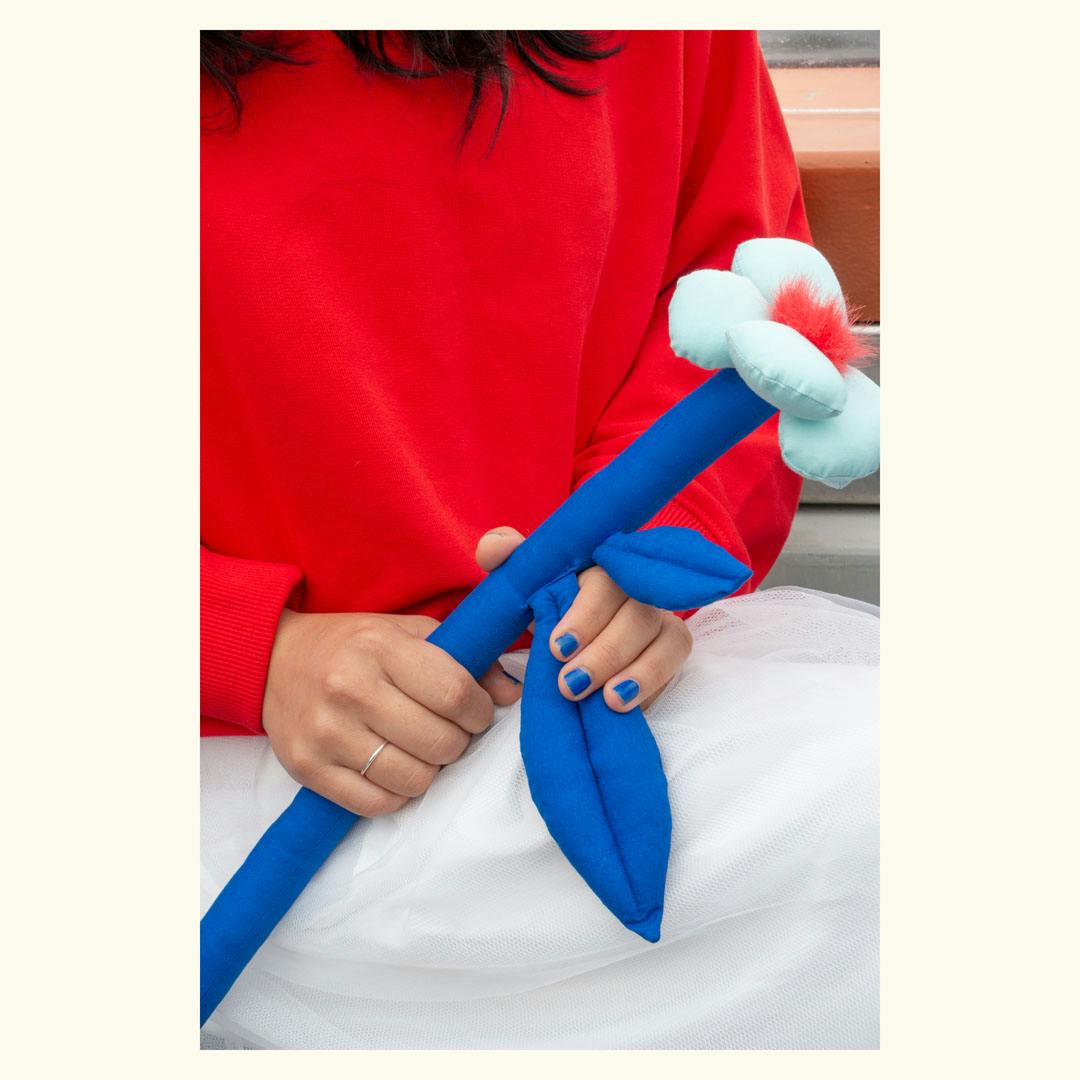 Person wearing a red top and white skirt holding a blue fabric flower with two leaves