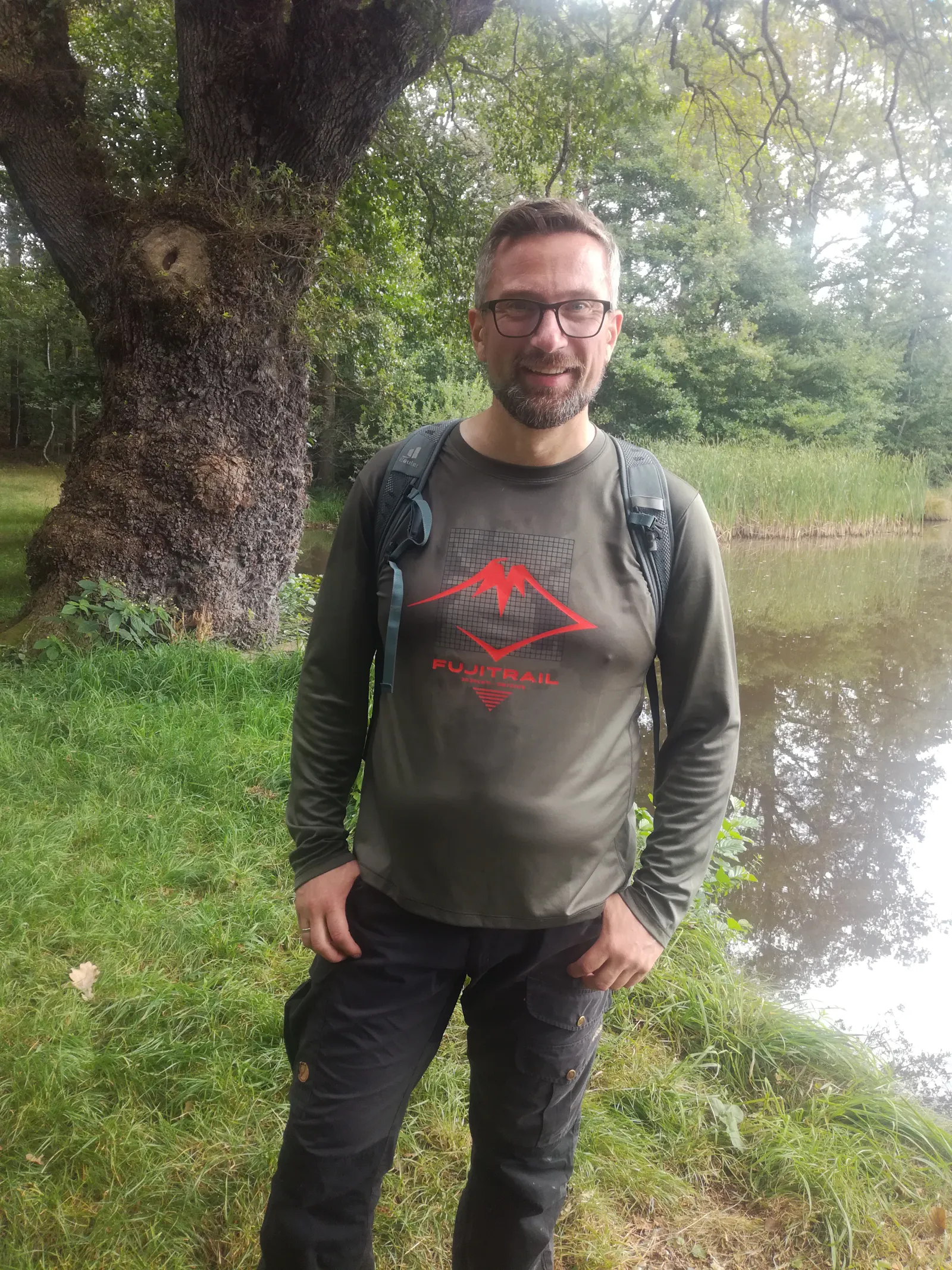 Martin Dulig im Wander-Outfit vor einem Teich und einem alten Baum.