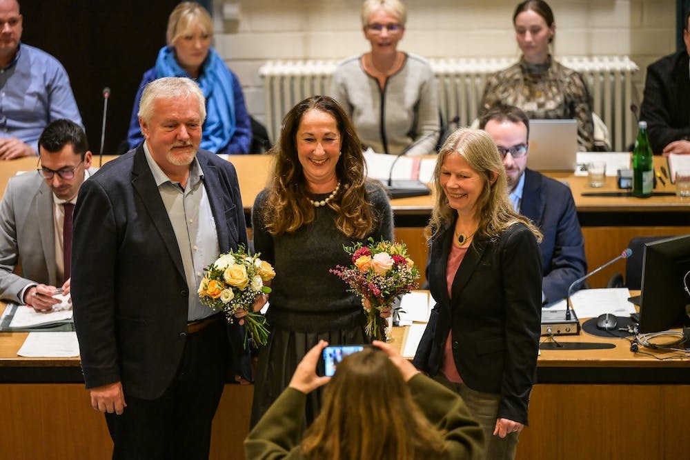 Herdeckes Bürgermeisterin Iris Stalzer (SPD) bei der Amtseinführung im Rathaus Herdecke. Sie steht zwischen zwei Personen, hält zwei Blumensträuße in der Hand, und lächelt in die Kamera.