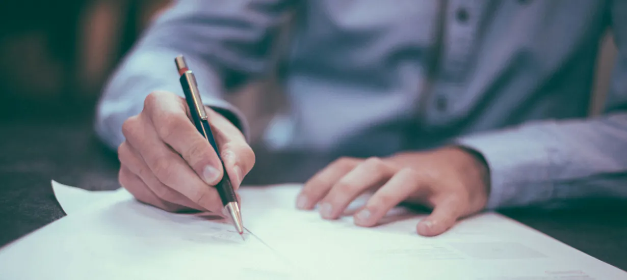 Image shows man signing a form