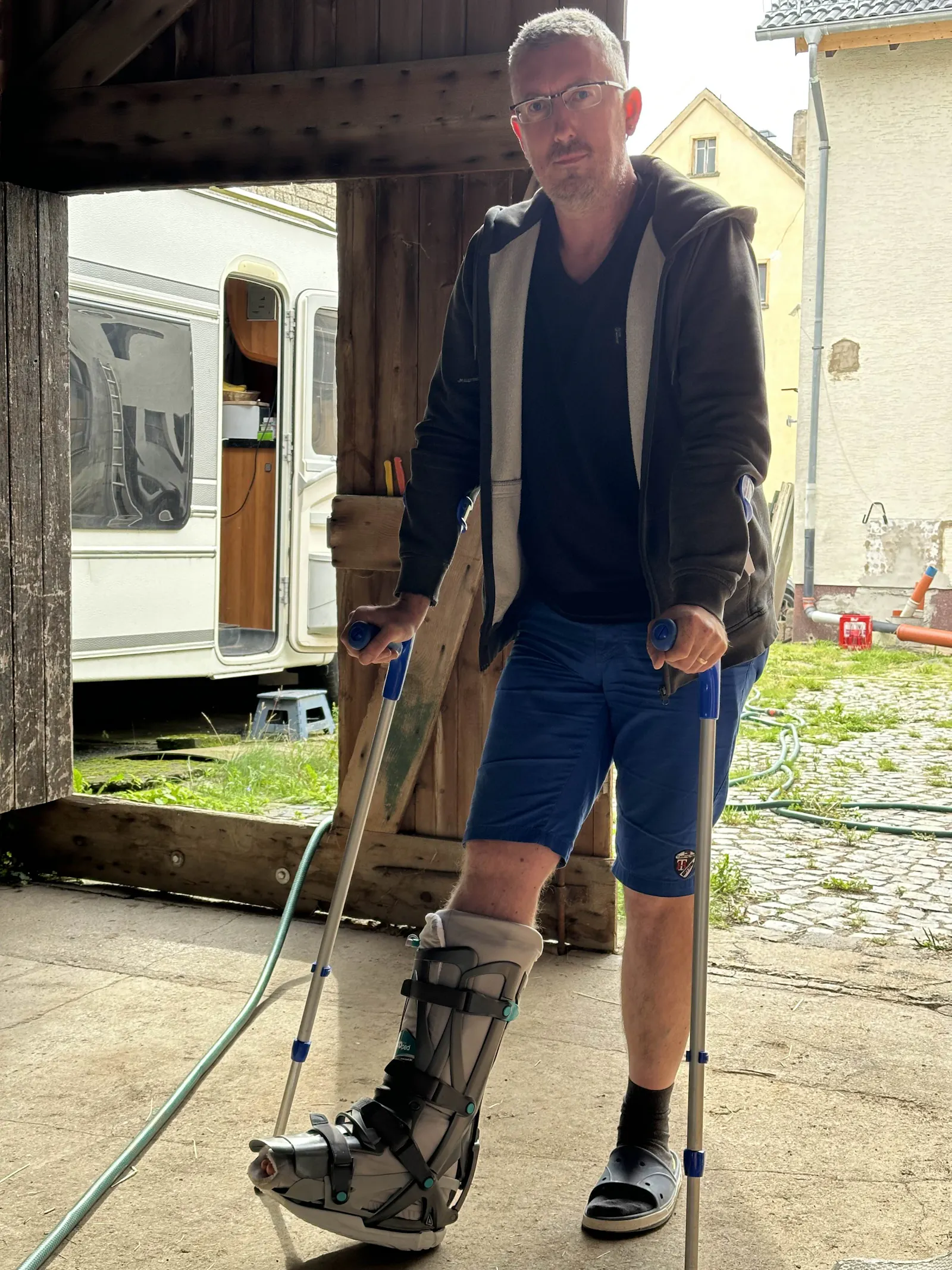 Aylins Mann mit zwei Krücken. Sein rechter Fuß steckt in einer großen grauen Orthese.