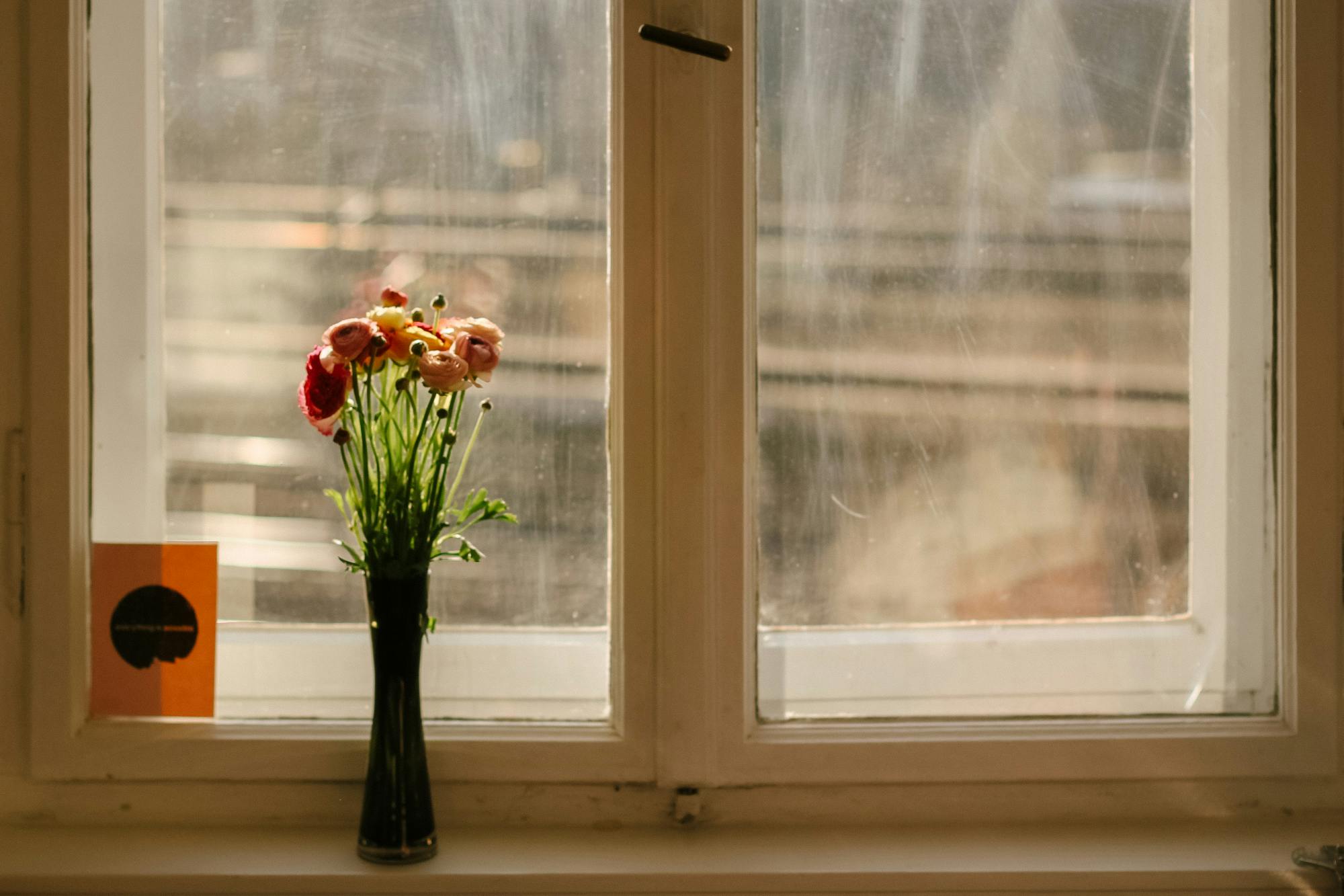 Vase mit bunten Blumen auf einer Fensterbank, dahinter der Blick auf Bahngleise.