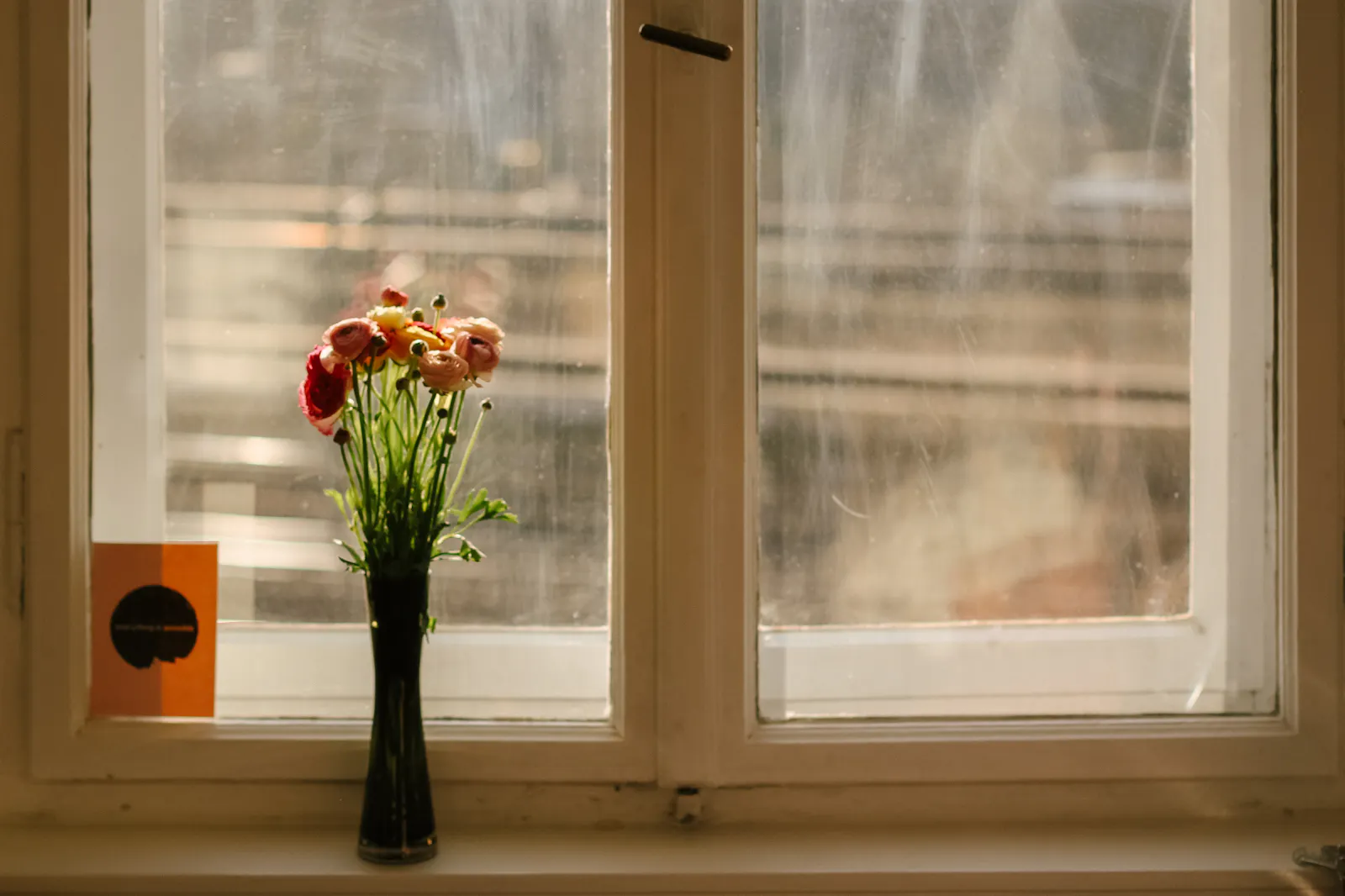 Vase mit bunten Blumen auf einer Fensterbank, dahinter der Blick auf Bahngleise.