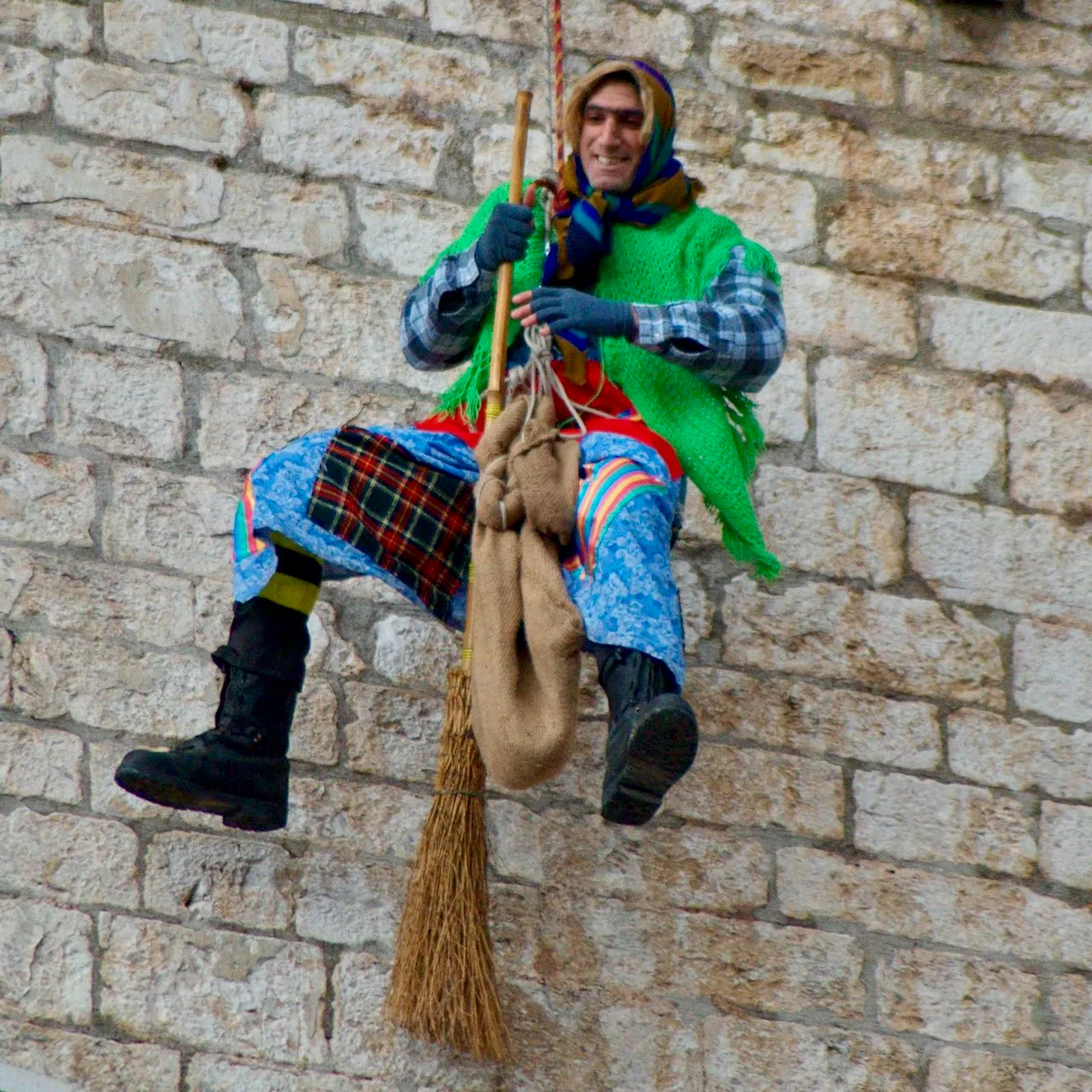 Eine erkennbar männliche Befana-Figur, die in der Nähe einer Mauer in der Luft hängt