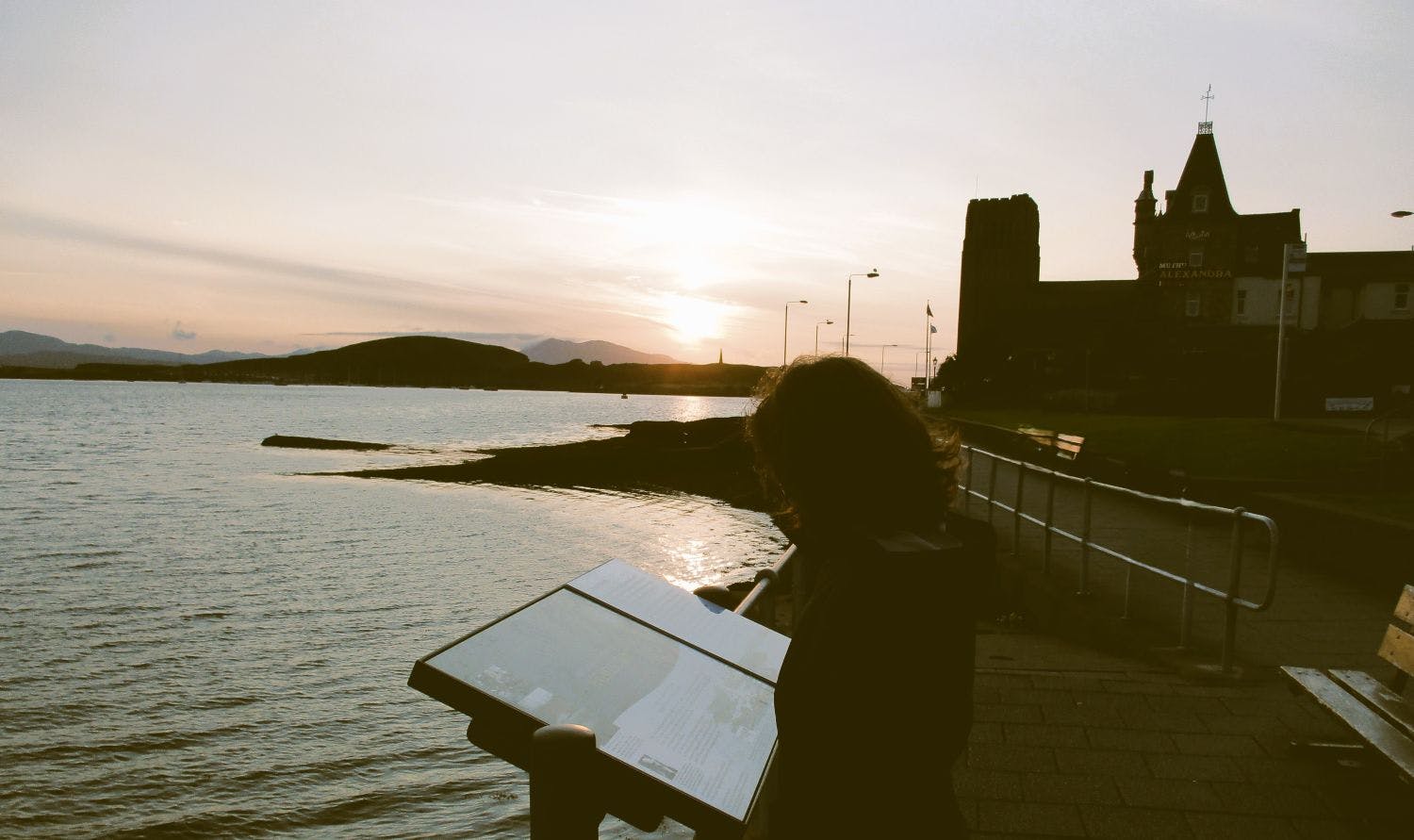 Eine Person steht an einer Küste im Sonnenuntergang und liest eine Tafel.