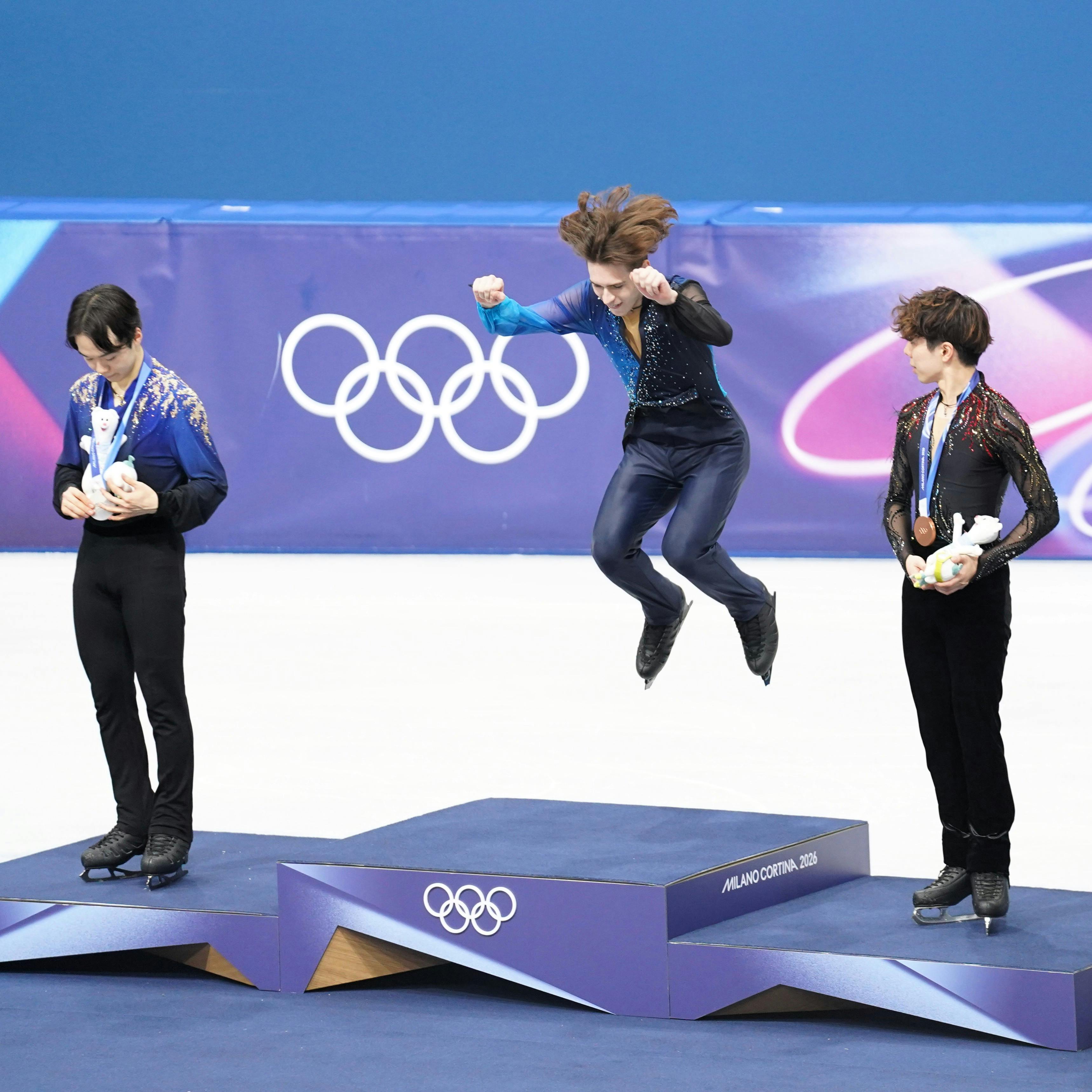 Mikhail Shaidorov springt auf das olympische Podium, links und rechts stehen Yuma Kagiyama und Shun Sato.