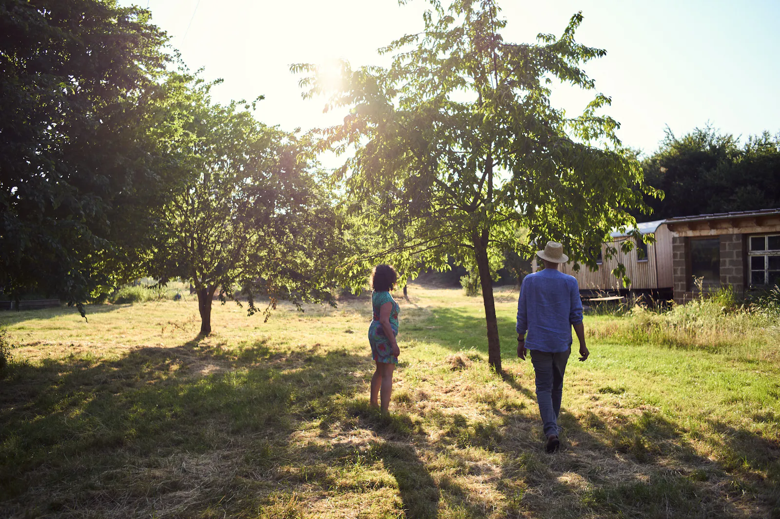 Josef und Carola gehen über den Thalhof der Sonne entgegen, die durch die Obstbäume scheint.