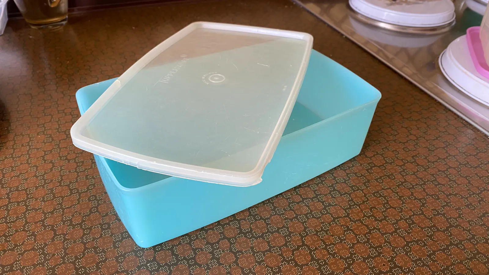 Eine hellblaue Tupperdose, auf der ein weißer, halbtransparenter Deckel liegt. Die Dose steht auf einer Küchenarbeitsplatte, rechts sind noch Teile des Herds zu sehen.
