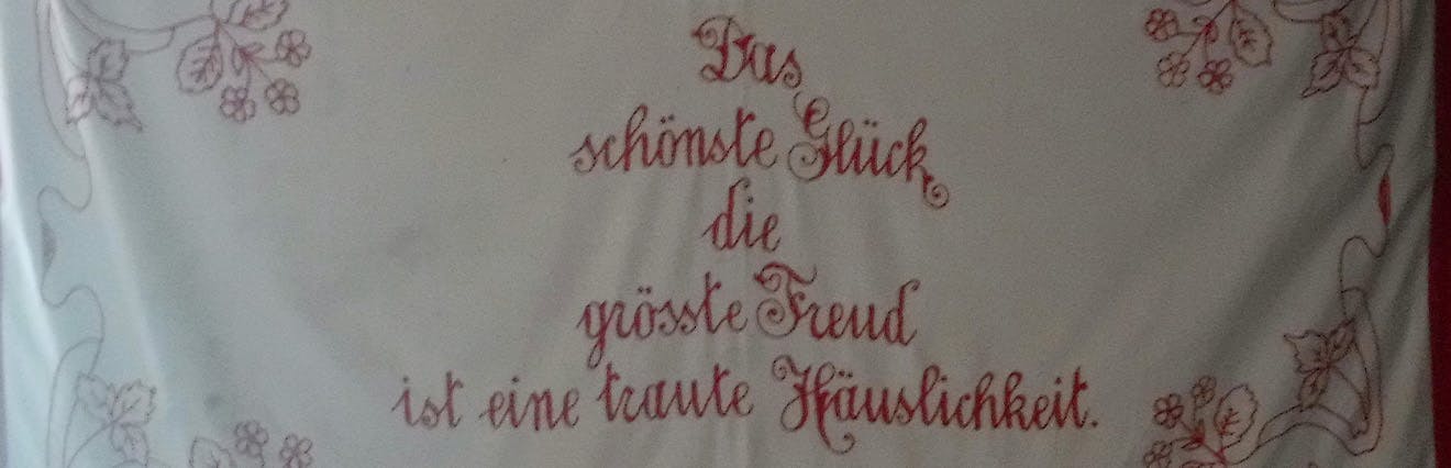 Besticktes Tuch mit dem Spruch "Das schönste Glück die grösste Freud ist eine traute Häuslichkeit"hi