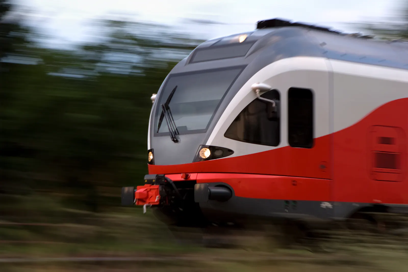 Das Bild zeigt die Frontansicht eines rot-weißen Zuges in voller Fahrt, der Hintergrund ist durch die Bewegung unscharf.