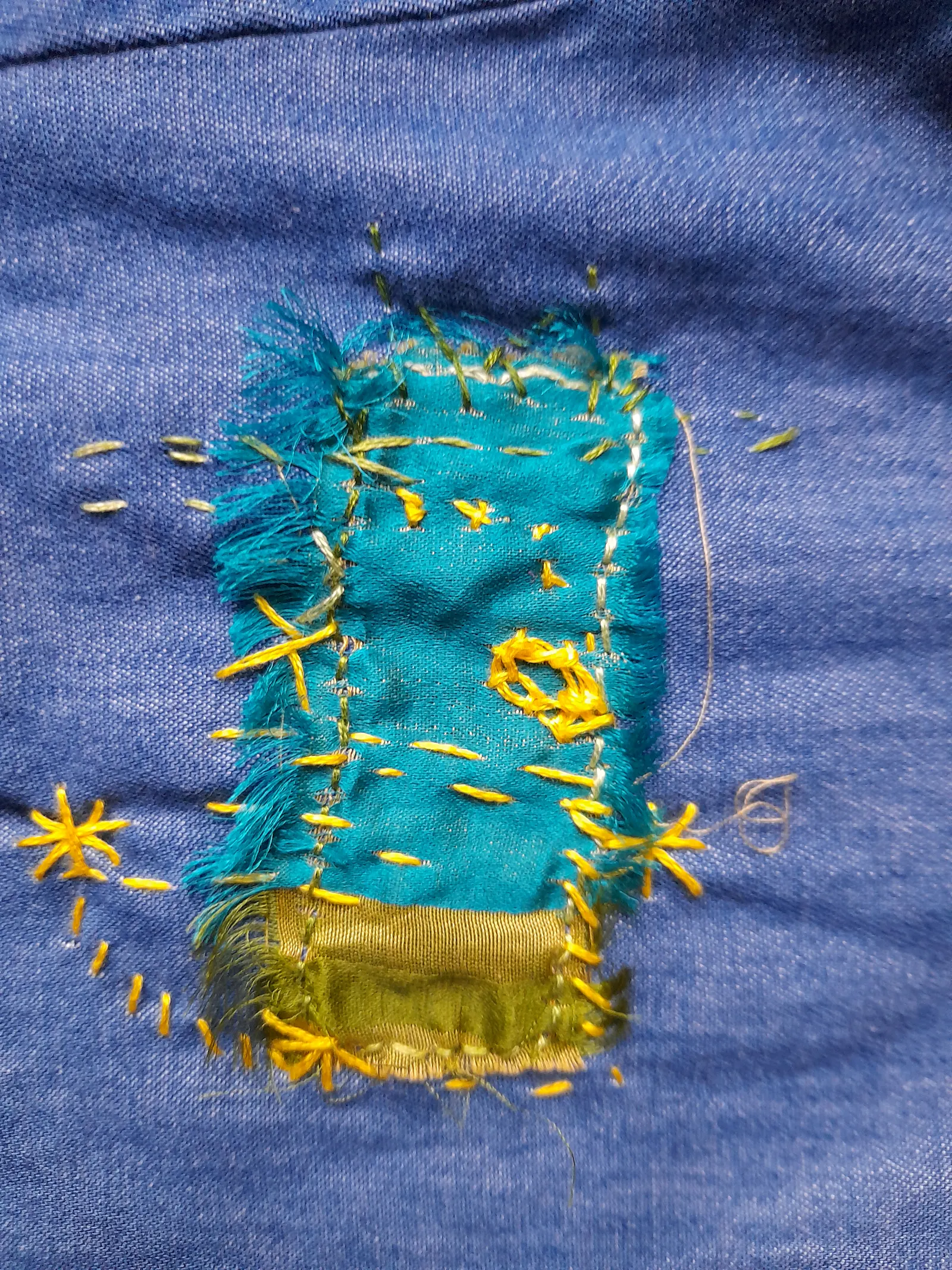 Blue jeans fabric with a colourful patch of turquoise and golden-yellow silk. Wild embroidery in yellow to fix the patch, with irregular stitches, some stars, a cross. It's like painting with a needle.