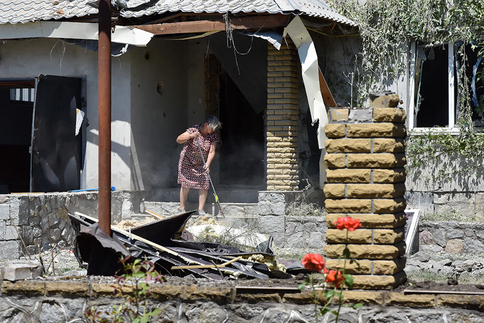 Ukrainerin fegt vor ihrem durch russische Raketen zerstörten Haus