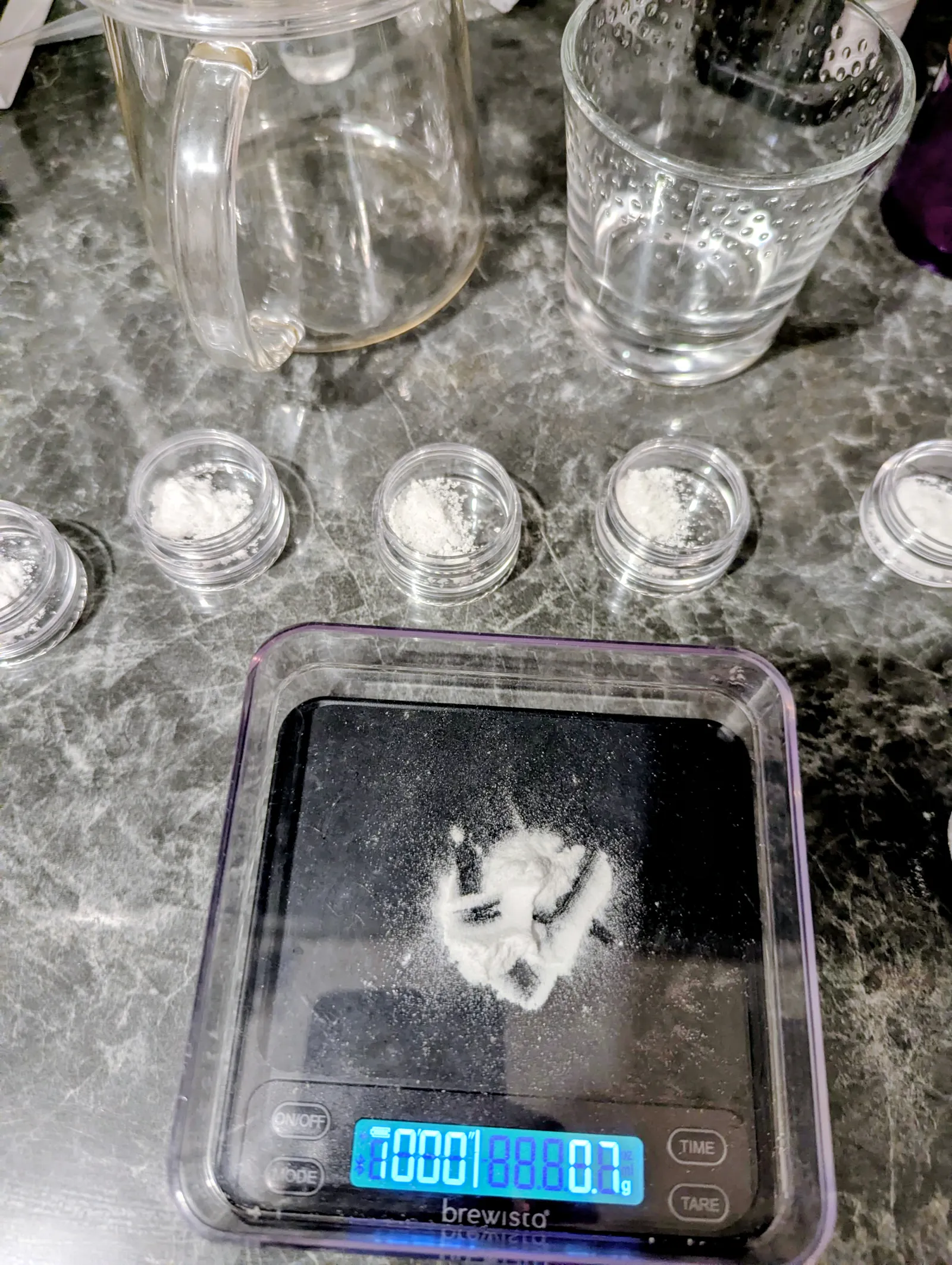 Eine Brewista-Präzisionswaage zeigt 0,7g Mineralienpulver an. Umgeben von kleinen Behältern mit Pulver unterstreicht dieses Bild die Notwendigkeit von Exaktheit, um das volle Aromenspektrum des Kaffees freizusetzen. Es ist Handwerk, kein Voodoo.
