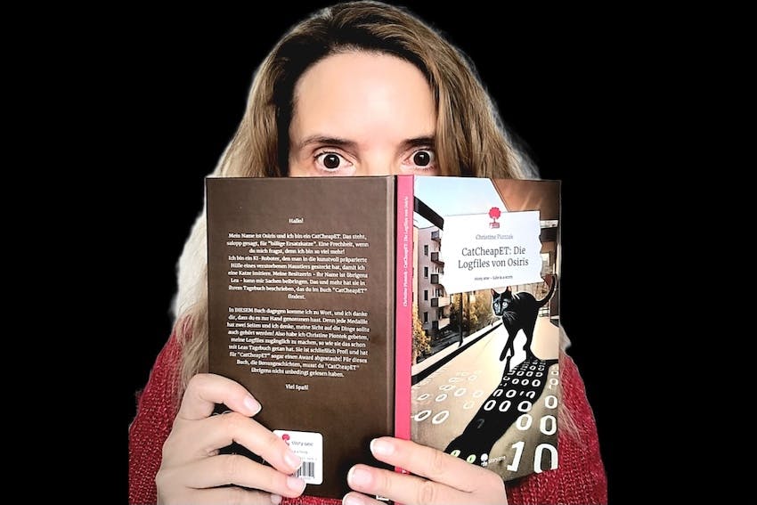 Christine Piontek mit ihrem Buch "CatCheapET: Die Logfiles von Osiris", das sie aufgeschlagen vors Gesicht hält, sodass nur noch ihre erstaunten Augen zu sehen sind