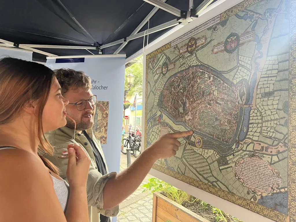 Zwei Menschen stehen vor dem alten Stadtplan von Duisburg aus dem 16. Jahrhundert und unterhalten sich.