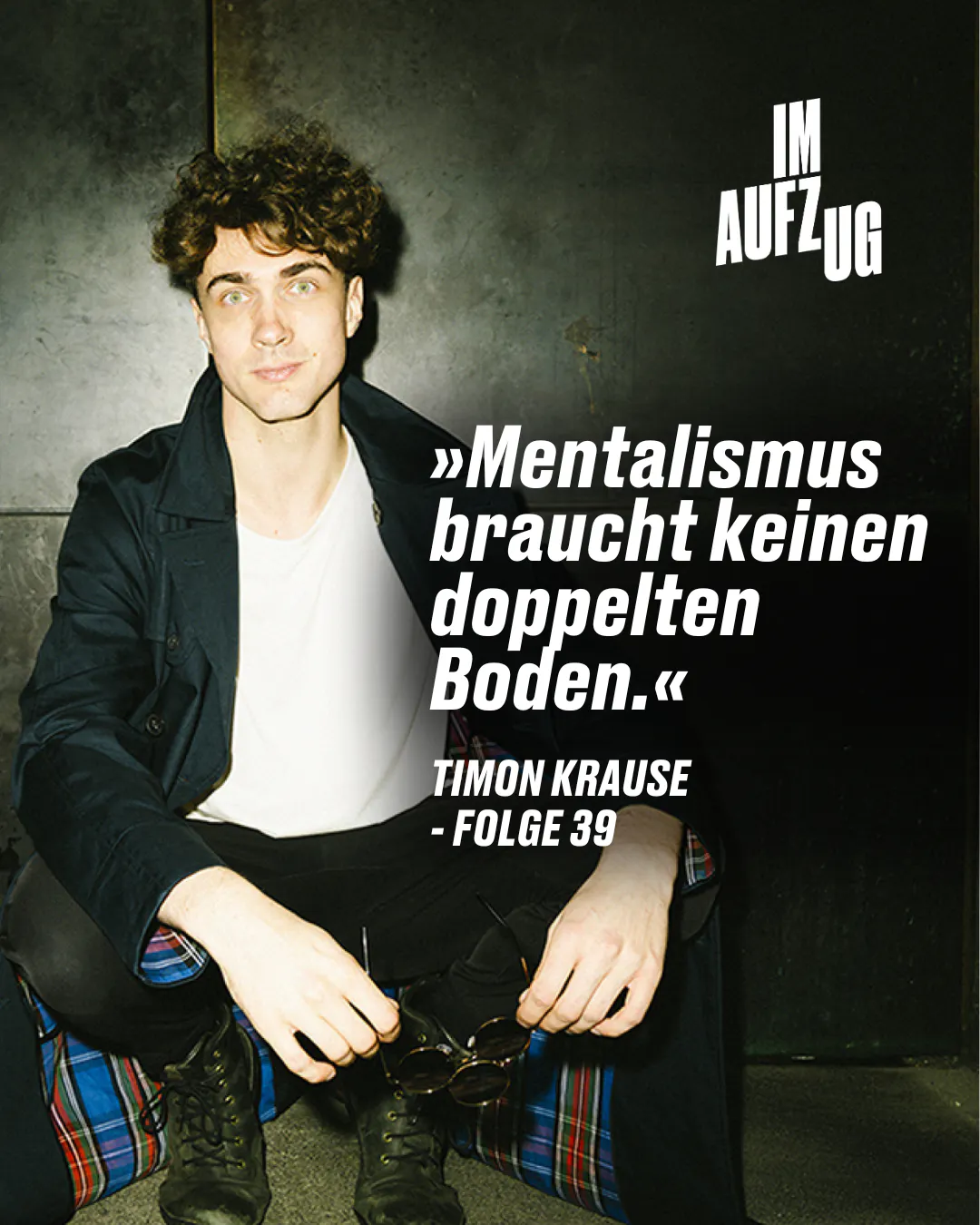 ALT-Text: Timon Krause, ein Mentalist, sitzt im Aufzug, lehnt an einer Metallwand und blickt direkt in die Kamera. Er trägt ein dunkles Jackett, ein weißes T-Shirt und eine Hose mit Karomuster. In seinen Händen hält er eine Sonnenbrille. Über ihm steht der Text: "Mentalismus braucht keinen doppelten Boden." - TIMON KRAUSE - FOLGE 39.