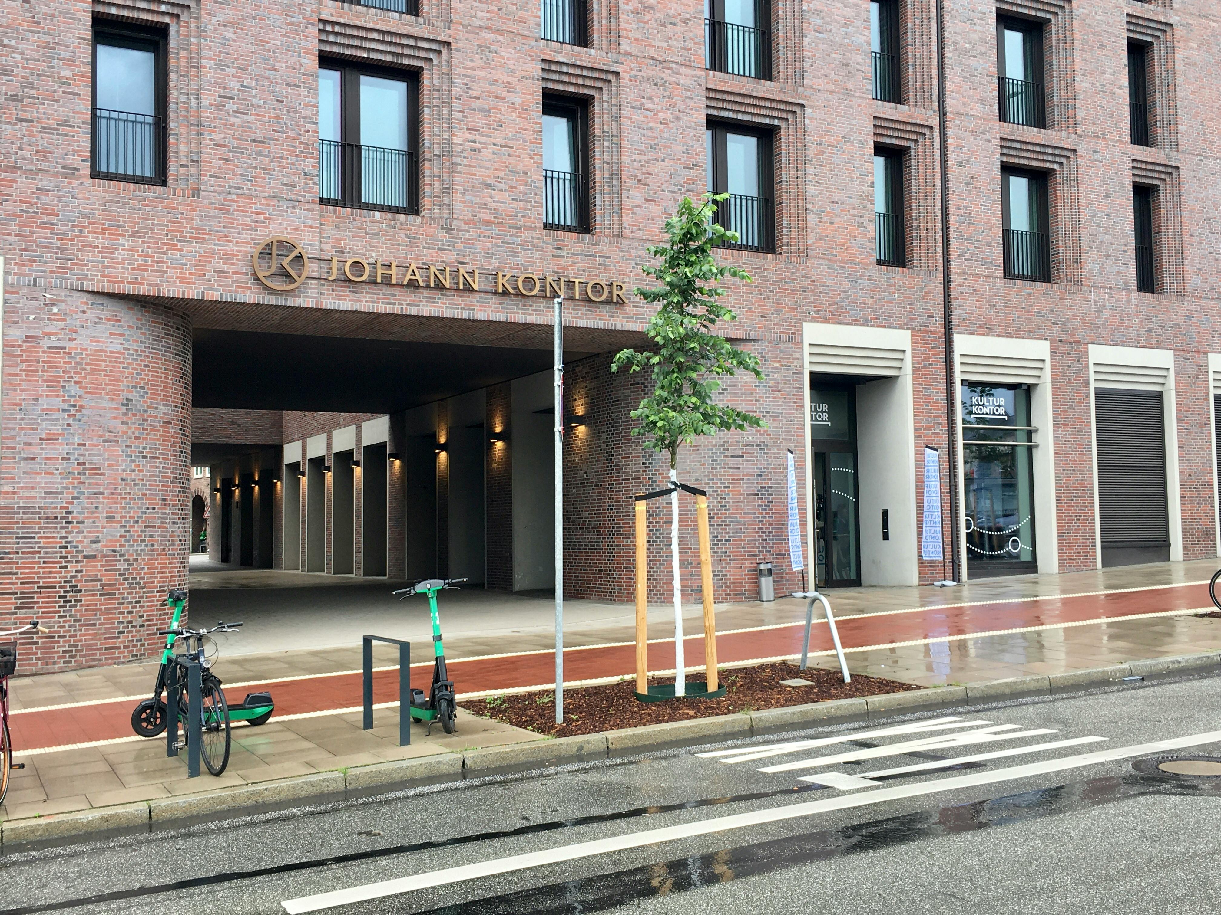 Bürogebäude "Johann Kontor", rechts der Eingang zum "Kultur Kontor", davor eine Straße, Fahrradständer und ein einzelner Baum.