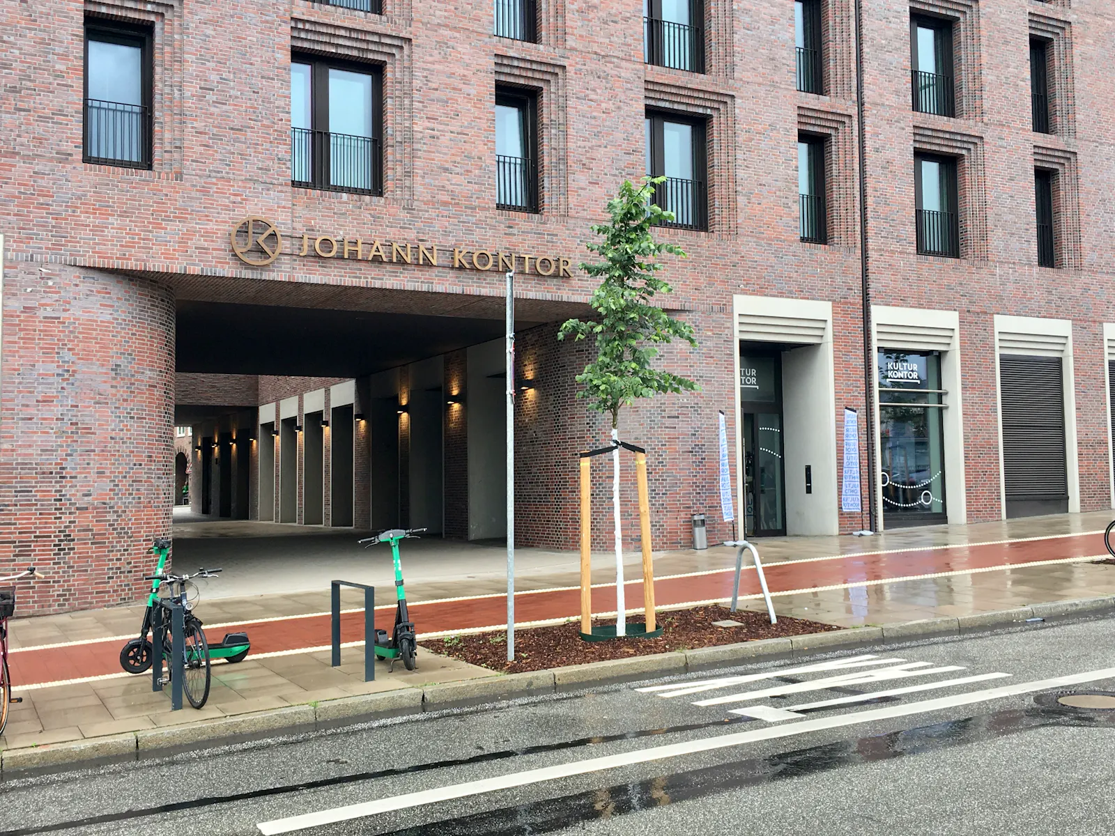 Bürogebäude "Johann Kontor", rechts der Eingang zum "Kultur Kontor", davor eine Straße, Fahrradständer und ein einzelner Baum.