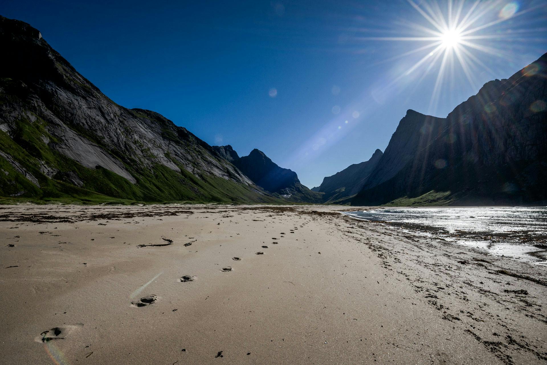 La plage au premier plan, avec une série de traces de pieds nus qui part au loin. En arrière-plan, les chaînes de montagne de la vallée, qui se rejoignent en un col tout au fond.