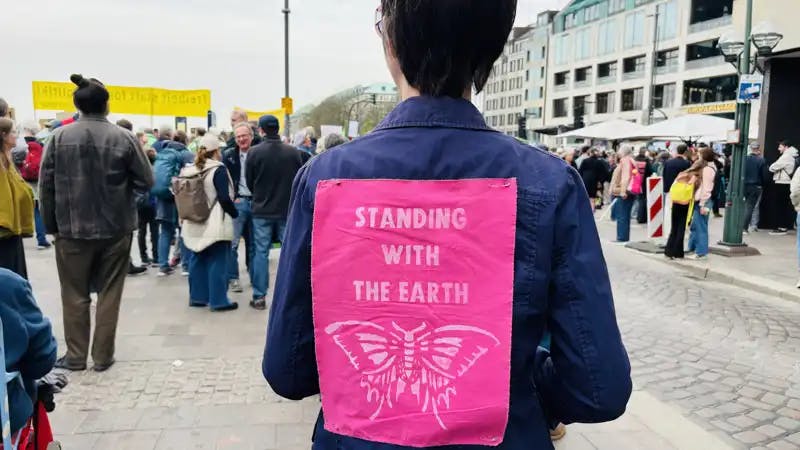 Demo-Teilnehmende von hinten mit einem Patch auf dem Rücken, auf dem steht "Standing with the earth".