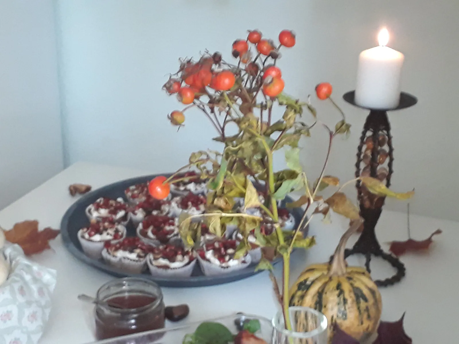 Herbstlich gedeckter Buffet-Tisch mit Kuchen, Kerze, Kürbis und Hagebuttenzweigen.