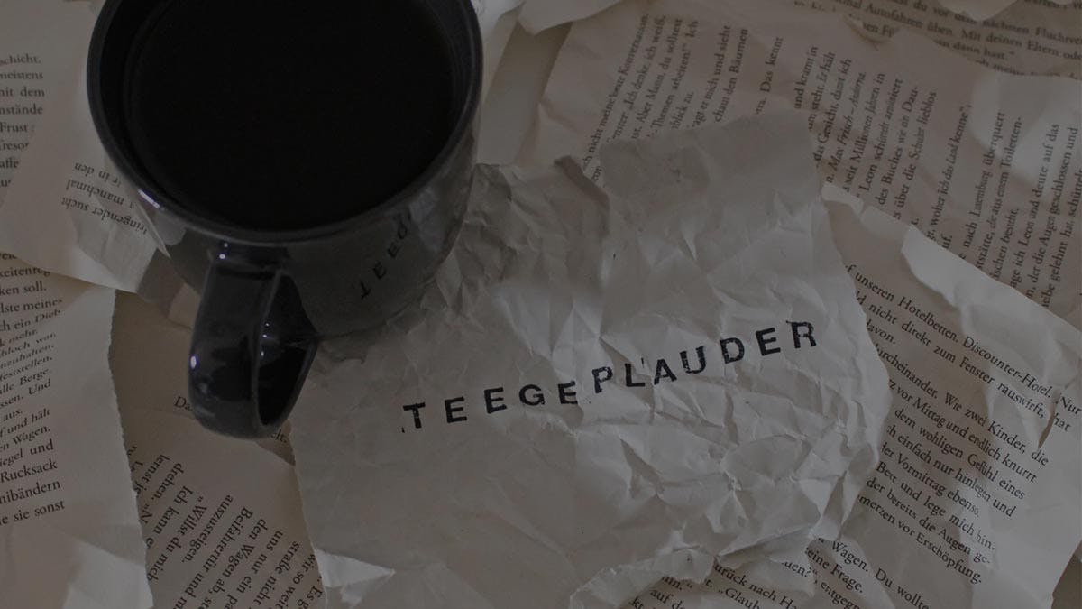 Zerknitterte Buchseiten, darauf eine Tasse mit Tee und daneben ein Zettel auf dem "Teegeplauder" steht.