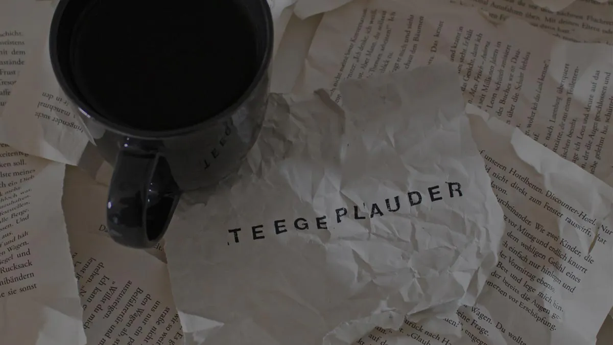 Zerknitterte Buchseiten, darauf eine Tasse mit Tee und daneben ein Zettel auf dem "Teegeplauder" steht.