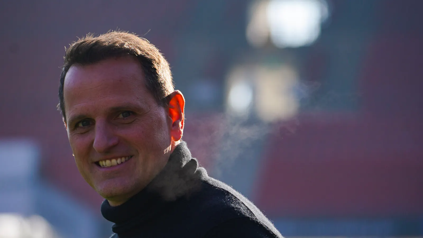 Joti Chatzialexiou, Sportvorstand vom 1. FC Nürnberg, lächelt in die Kamera. Hinter ihm sind verschwommen die Stadionsitze zu sehen.