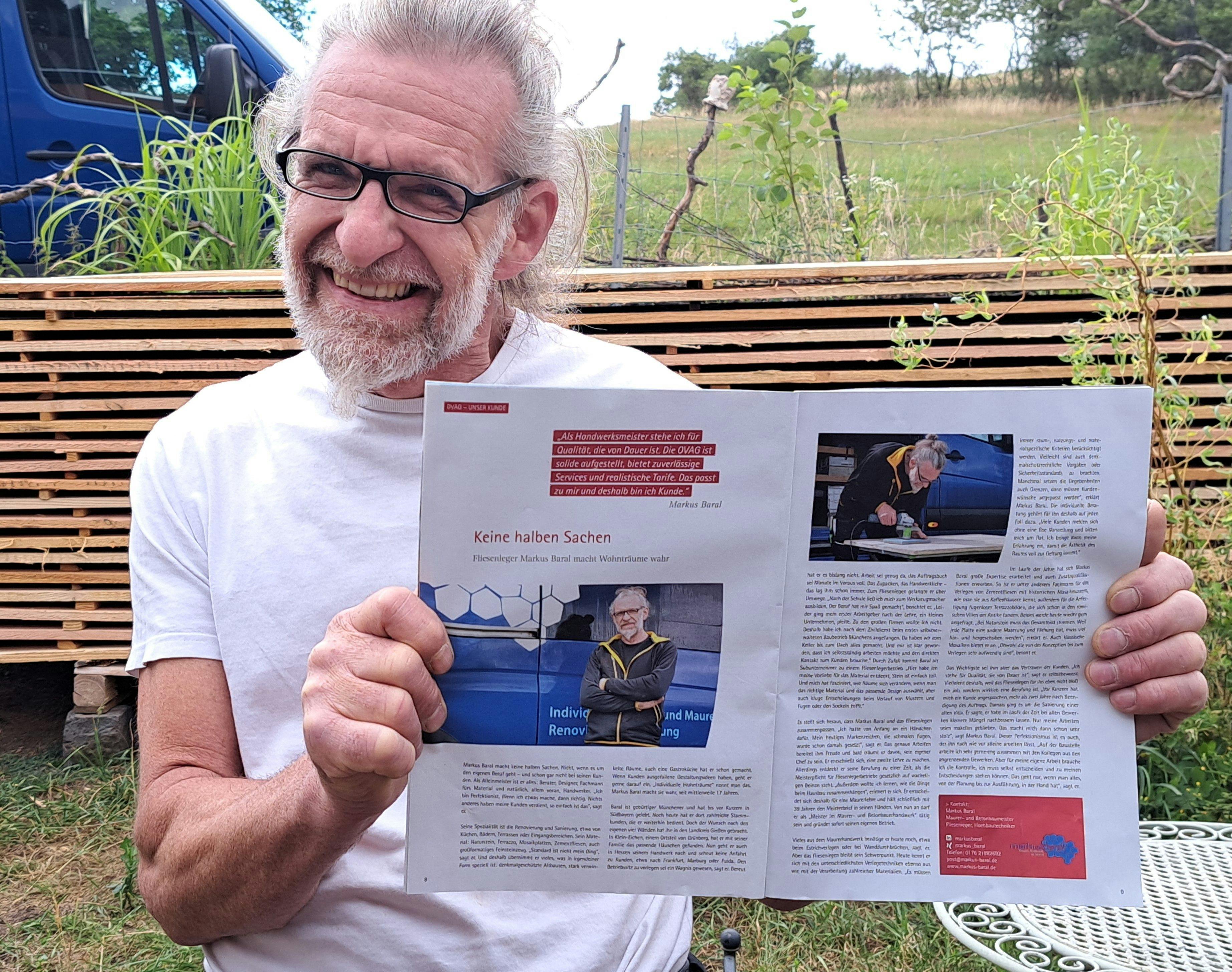 Foto zeigt Markus Baral, lachend, eine Ausgabe des Magazins "Unser Oberhessen" in den Händen haltend, aufgeschlagen bei dem Artikel "Keine halben Sachen: Fliesenleger Markus Baral macht Wohnträume wahr".