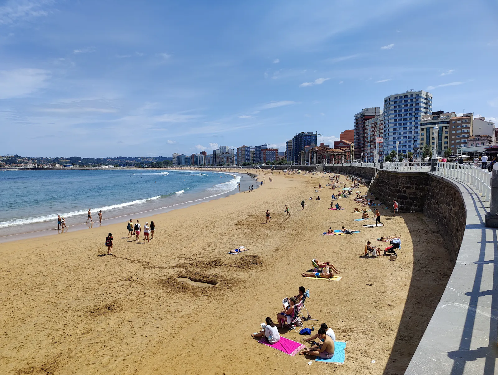San Lorenzo beach with sunbathers and swimmers, framed by the seaside promenade and the city’s modern skyline | Calle Cabrales 2, 33201 Gijón/Xixón