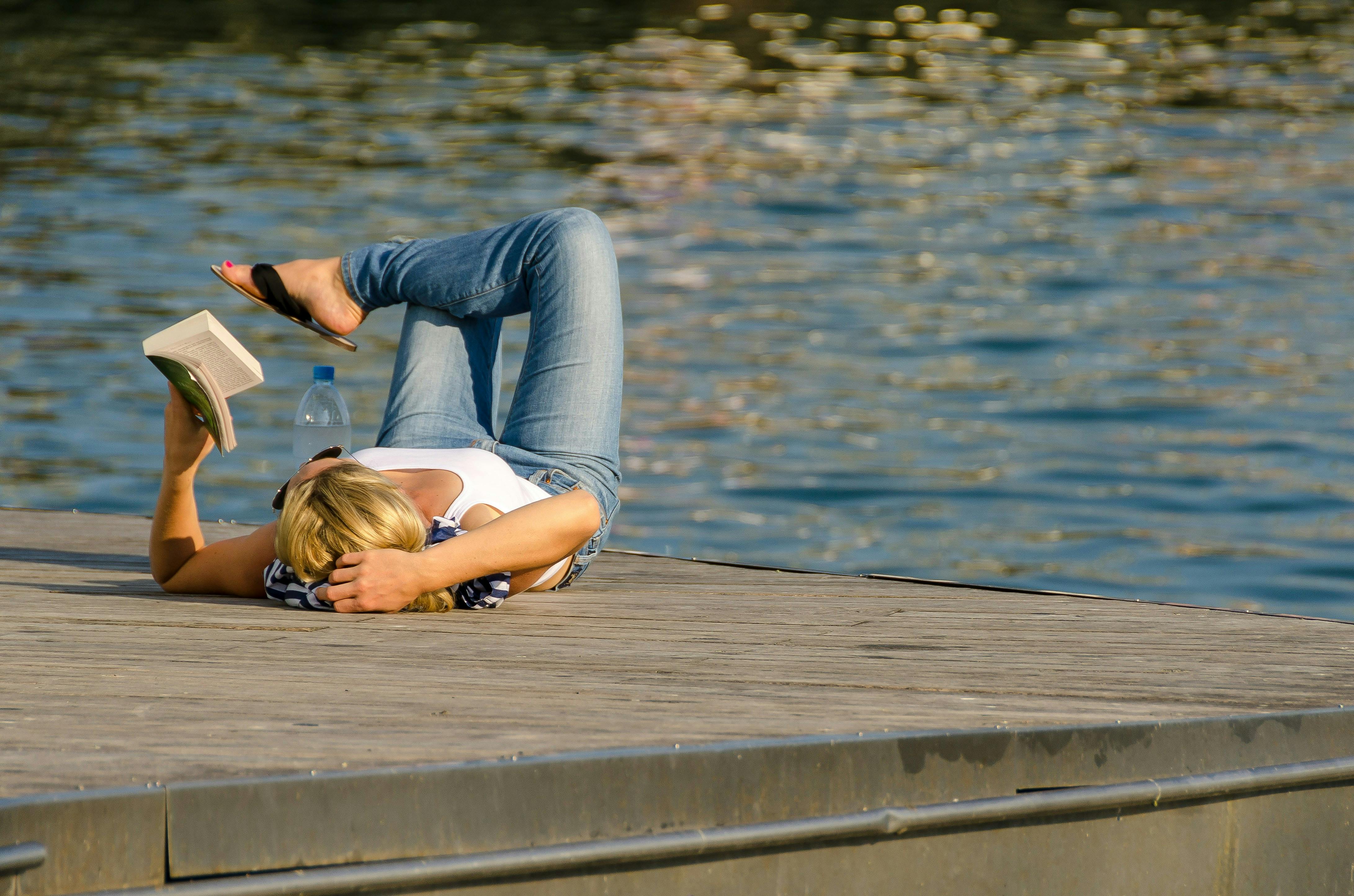 Eine Frau liegt an einem See und liest ein Buch.
