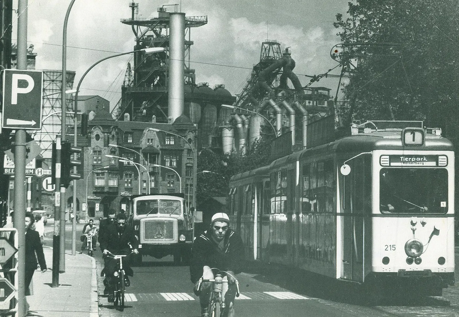 Großstädtische Straßenszene mit Straßenbahn, Lastwagen, Fahrradfahrern und Fußgängern. Das Bild ist so aufgenommen, dass alle auf einen zu kommen. Im Hintergrund das Stahlwerk Thyssen.