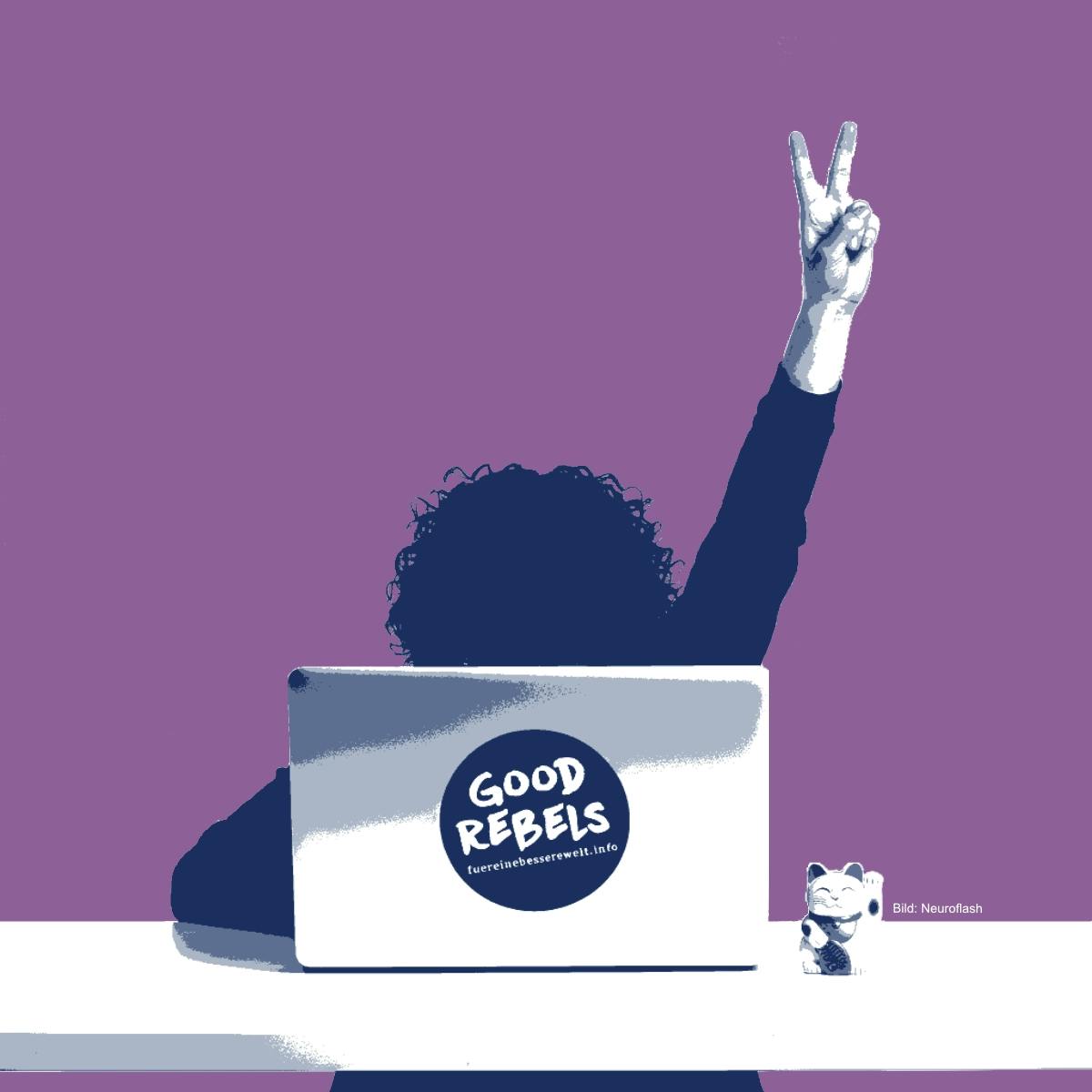 [Eine Frau sitzt hinter ihrem Laptop, auf dem ein GOOD-REBELS-Aufkleber angebracht ist, und hebt ihre Hand zum Victory-Zeichen]