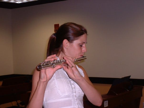 Danielle in the mid-2000s wearing a white blouse and playing the flute. Her brown hair is in a ponytail as she plays from a page of sheet music.
