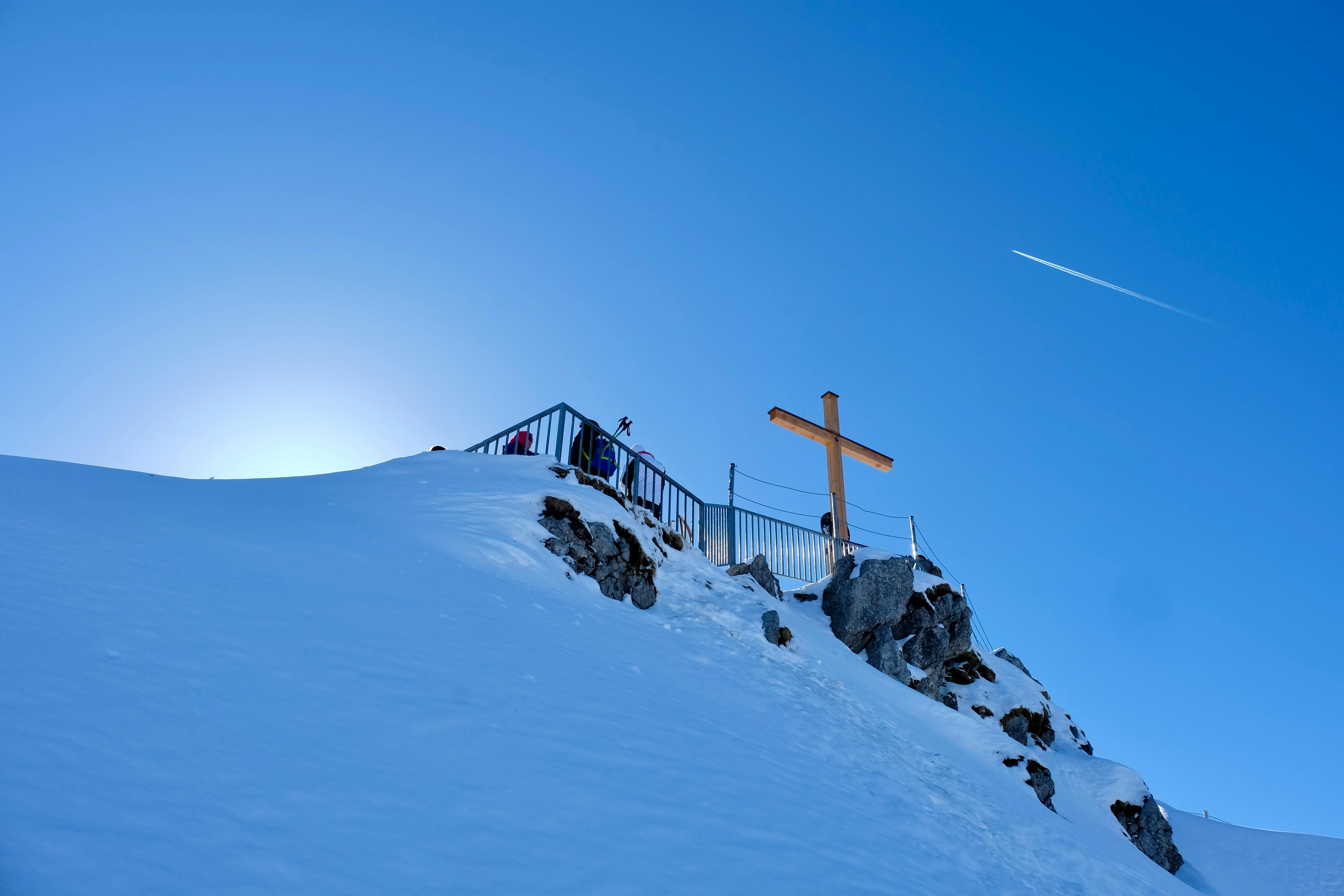 Blick auf eine schneebedeckte Bergspitze mit Gipfelkreuz und blauem Himmel im Hintergrund.