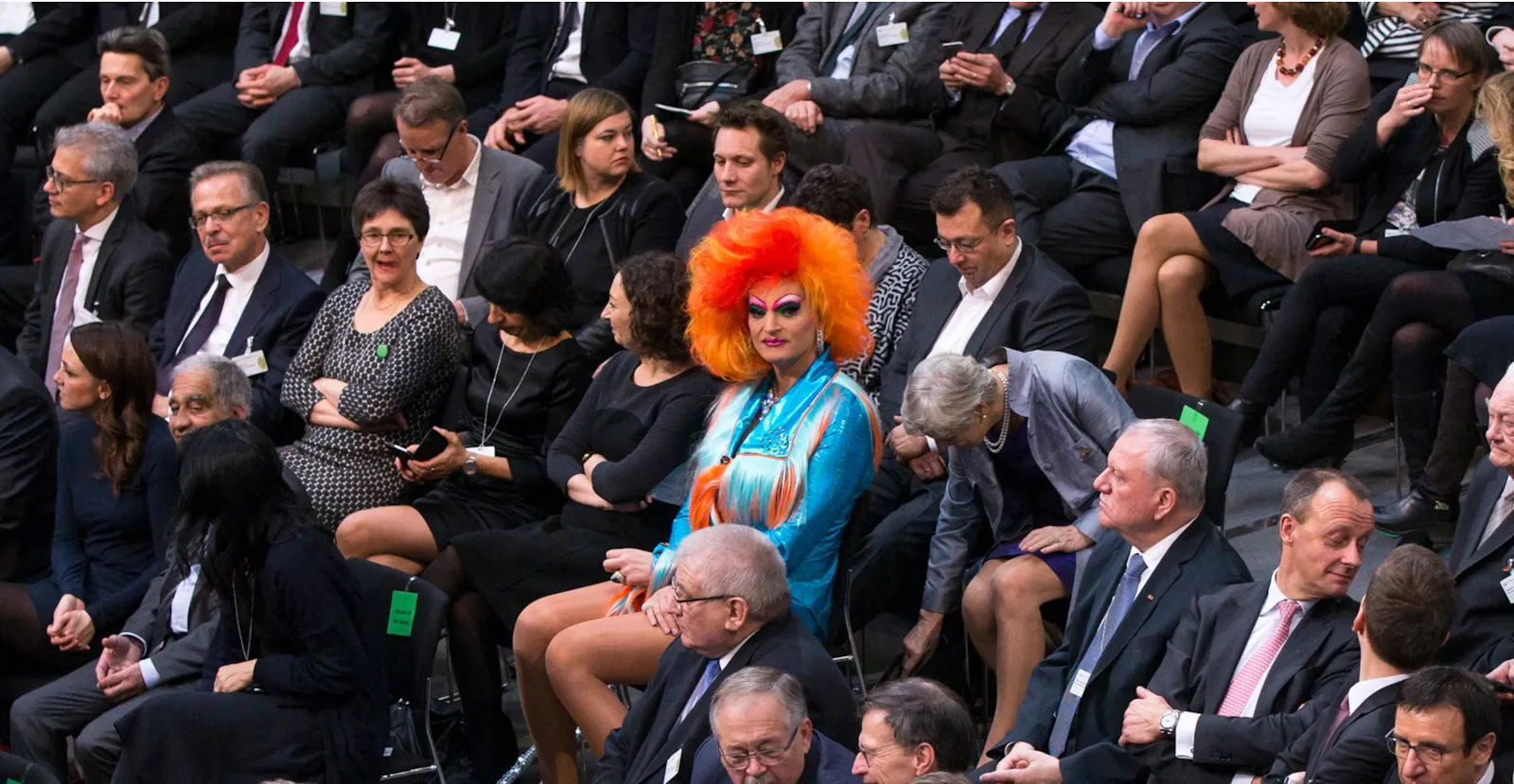Ein Termin mit Bundestagspolitiker*innen und anderen, fast nur Männer in grauen und schwarzen Anzügen. Mittendrin eine kunterbunt gekleidete Transfrau mit riesig auftoupierten orangefarbenen Haaren.
