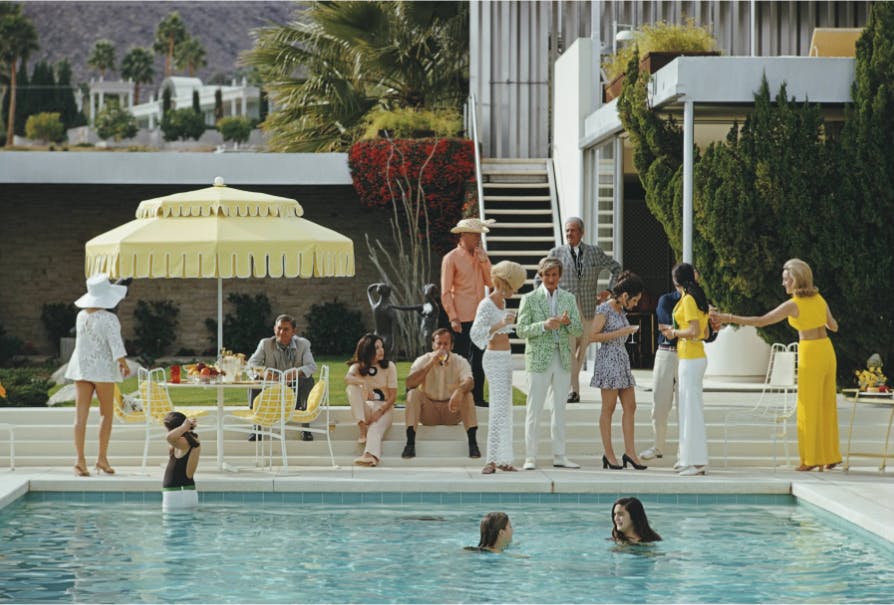 Menschen an einem Pool, im Hintergrund Palmen und eine Villa