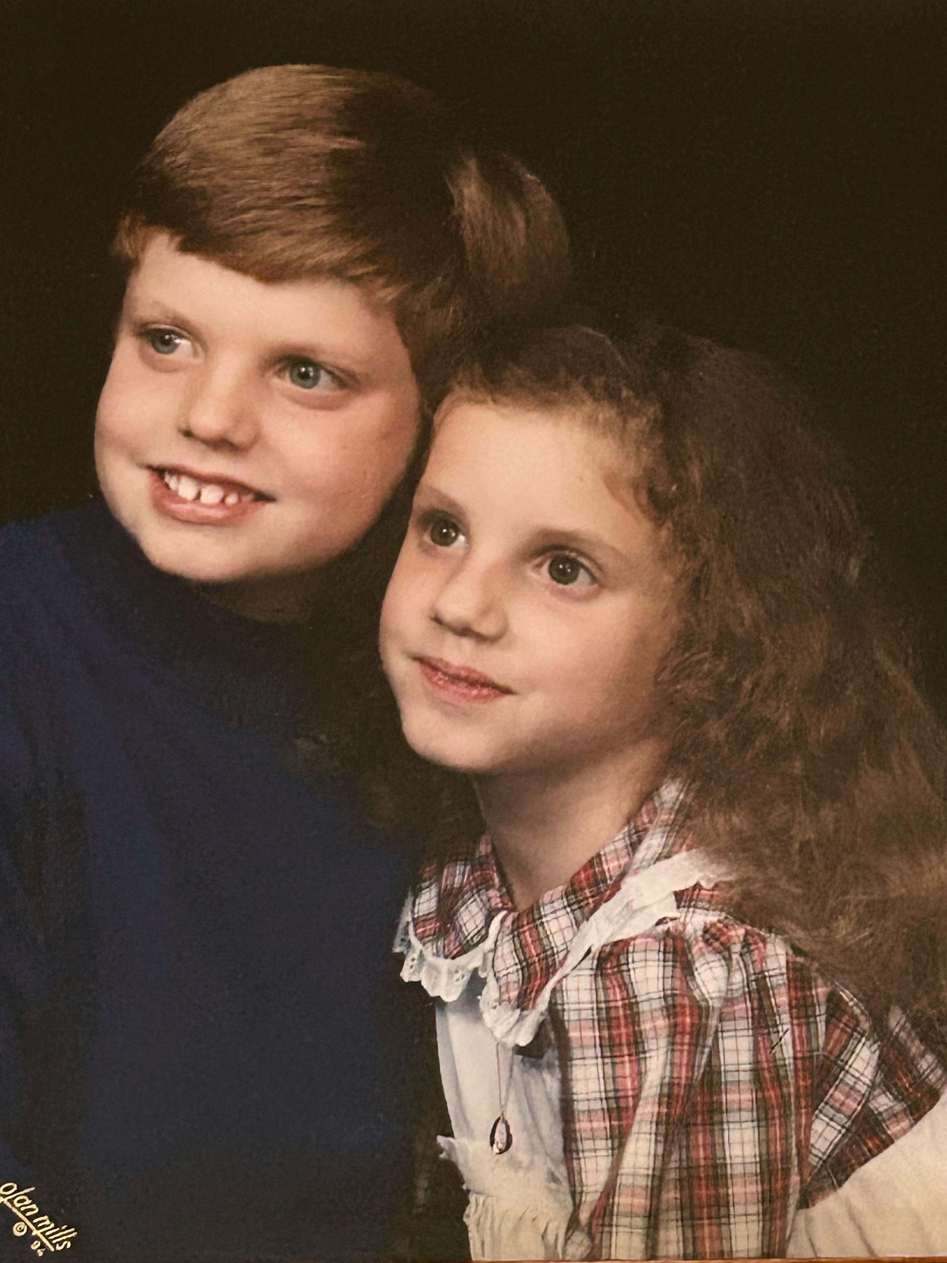 My sister and I in 1994 for a professional studio portrait. I’m on the left in a blue sweatshirt with a typical neat ‘90s haircut and an embarrassing overbite. My sister is beside me on the right with her brown hair loose, and wearing a white and red checkerboard patterned dress. She isn’t showing her teeth when smiling.