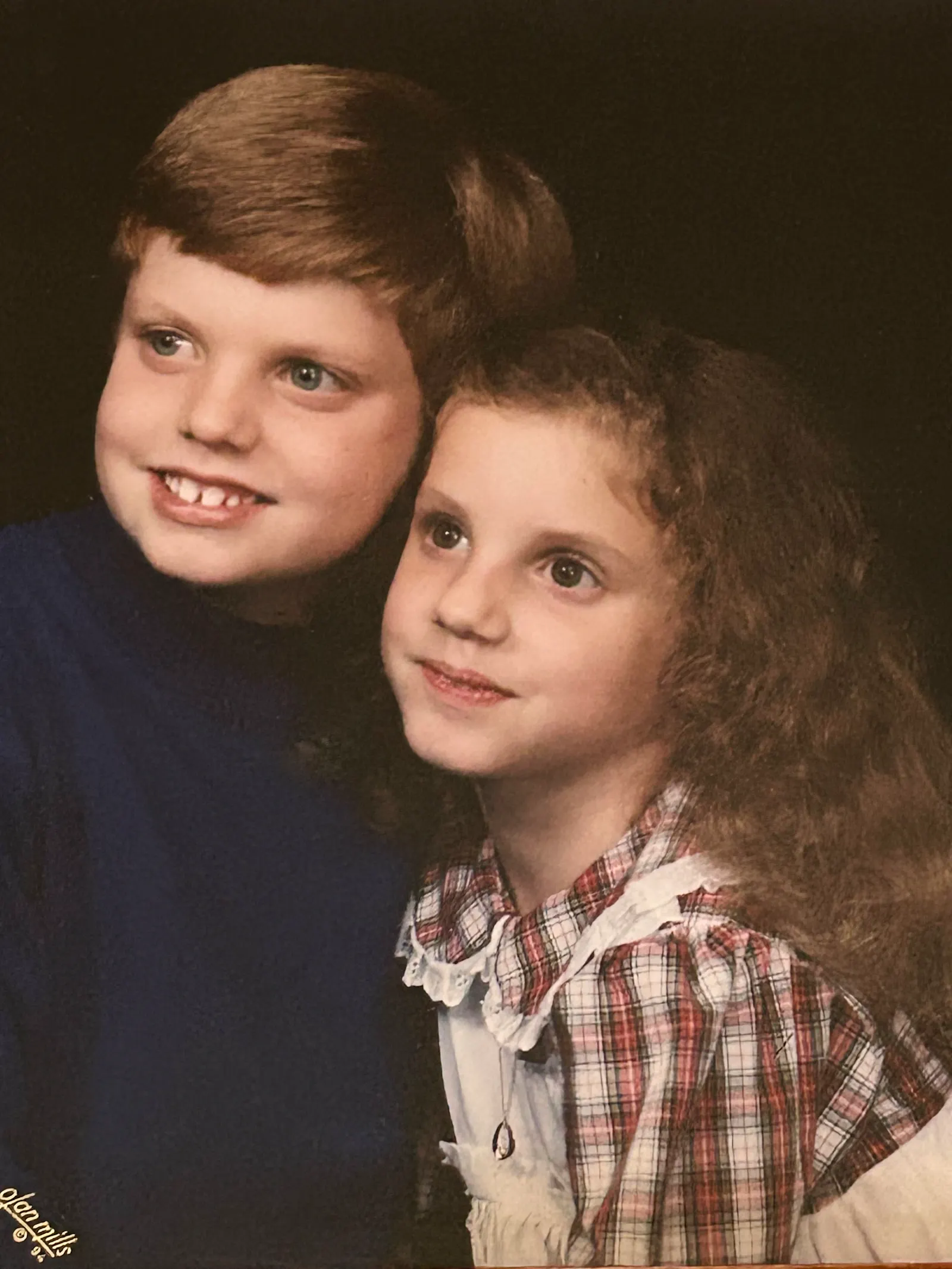 My sister and I in 1994 for a professional studio portrait. I’m on the left in a blue sweatshirt with a typical neat ‘90s haircut and an embarrassing overbite. My sister is beside me on the right with her brown hair loose, and wearing a white and red checkerboard patterned dress. She isn’t showing her teeth when smiling.