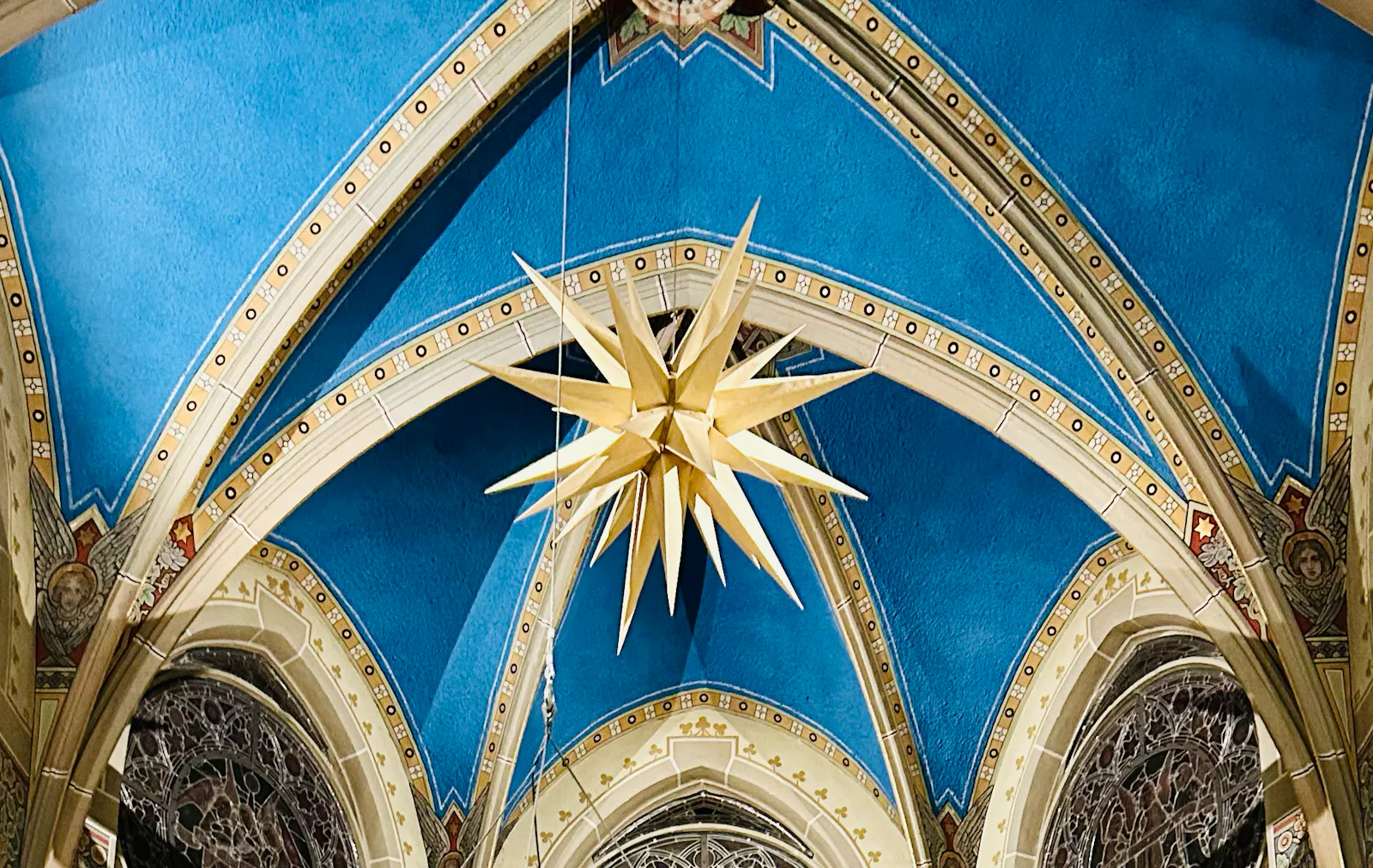 Ein hell leuchtender Weihnachtsstern hängt im Altargewölbe mit blauer Decke einer Kirche.