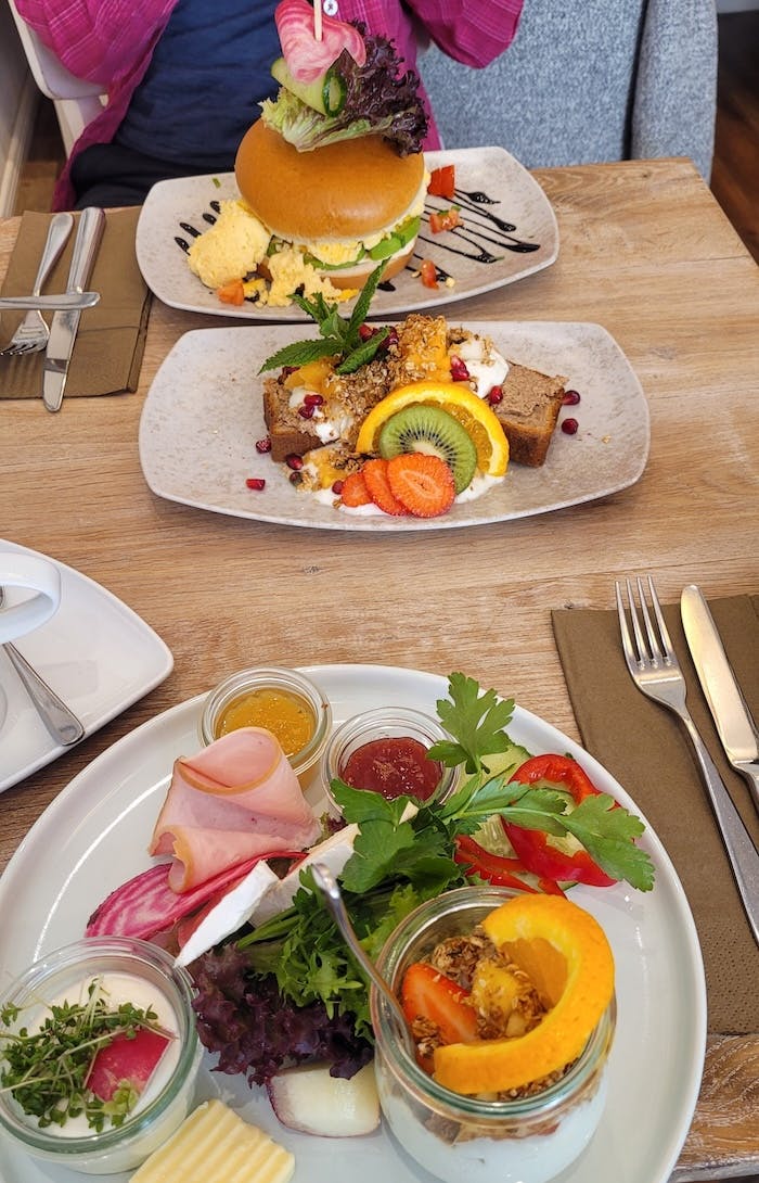 Frühstück im Café Zeitgeist in Lüneburg mit drei Tellern, auf denen unter anderem hausgebackenes Bananenbrot, viel Obst und frisches Gemüse zu sehen sind.