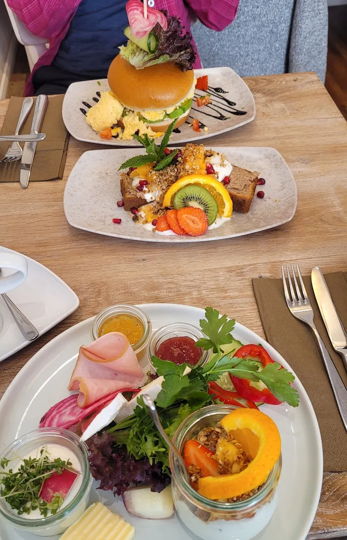 Frühstück im Café Zeitgeist in Lüneburg mit drei Tellern, auf denen unter anderem hausgebackenes Bananenbrot, viel Obst und frisches Gemüse zu sehen sind.