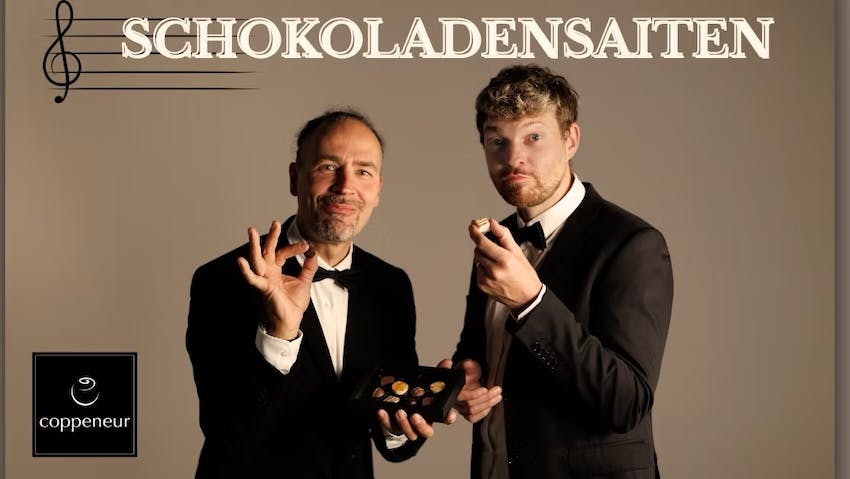 Eddi Hüneke und Tobi Hebbelmann essen im Smoking Pralinen. Motiv für das Konzert "Schokoladensaiten" in der Confiserie Coppeneuer.