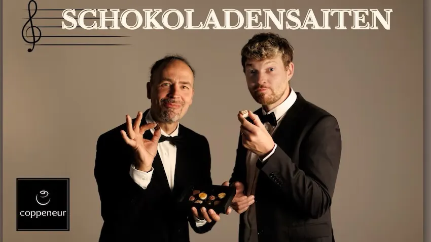 Eddi Hüneke und Tobi Hebbelmann essen im Smoking Pralinen. Motiv für das Konzert "Schokoladensaiten" in der Confiserie Coppeneuer.