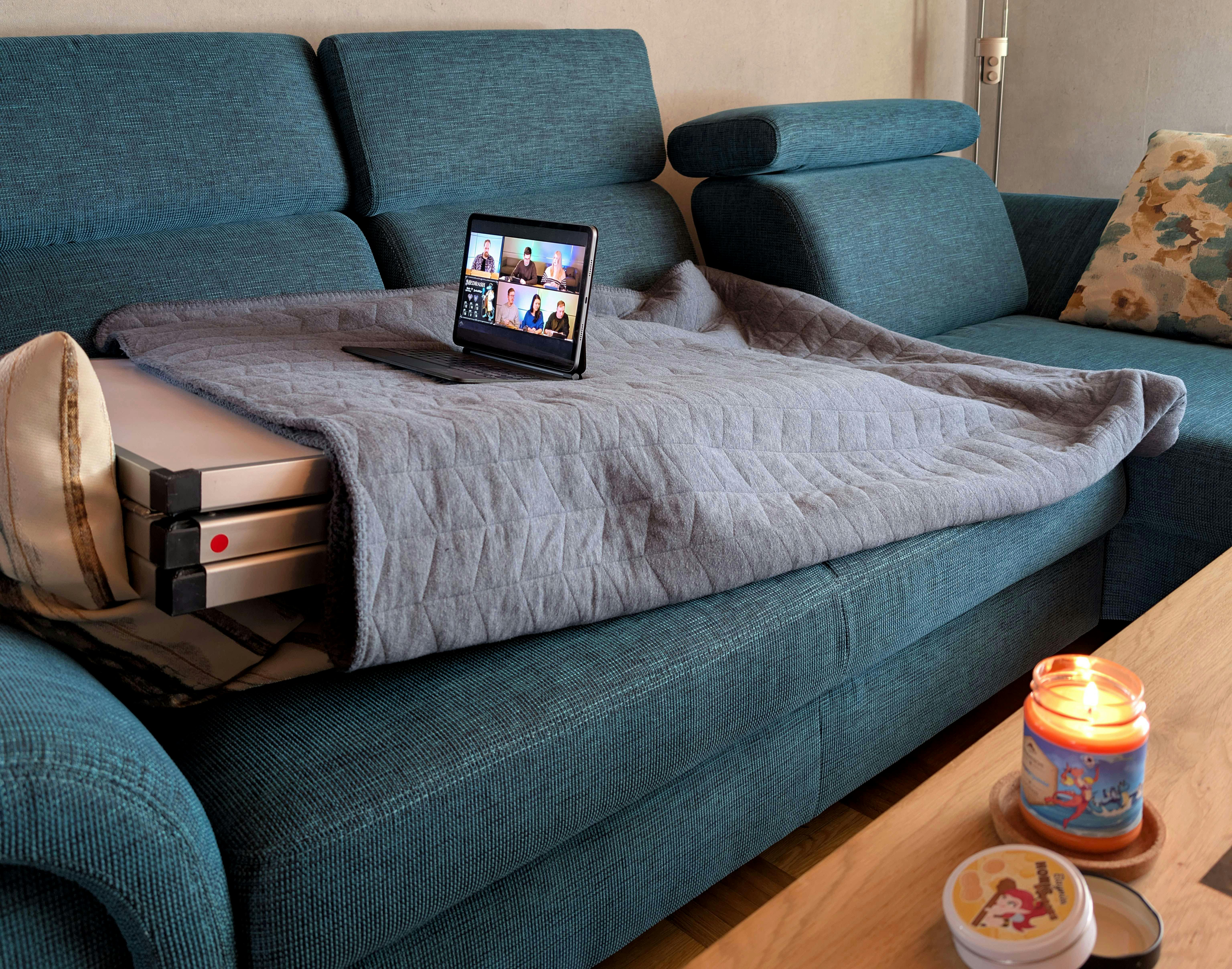 Der Tapeziertisch genießt das Leben in vollen Zügen: Er liegt auf dem Sofa, ist zugedeckt und schaut am Tablet die neueste Episode der Dice Actors. Nebenbei greift er bequem zum Tisch, um sich an Elaynies Honigbonbons zu bedienen und genießt den Duft sowie das Kerzenlicht der „Sommerpause“-Kerze.