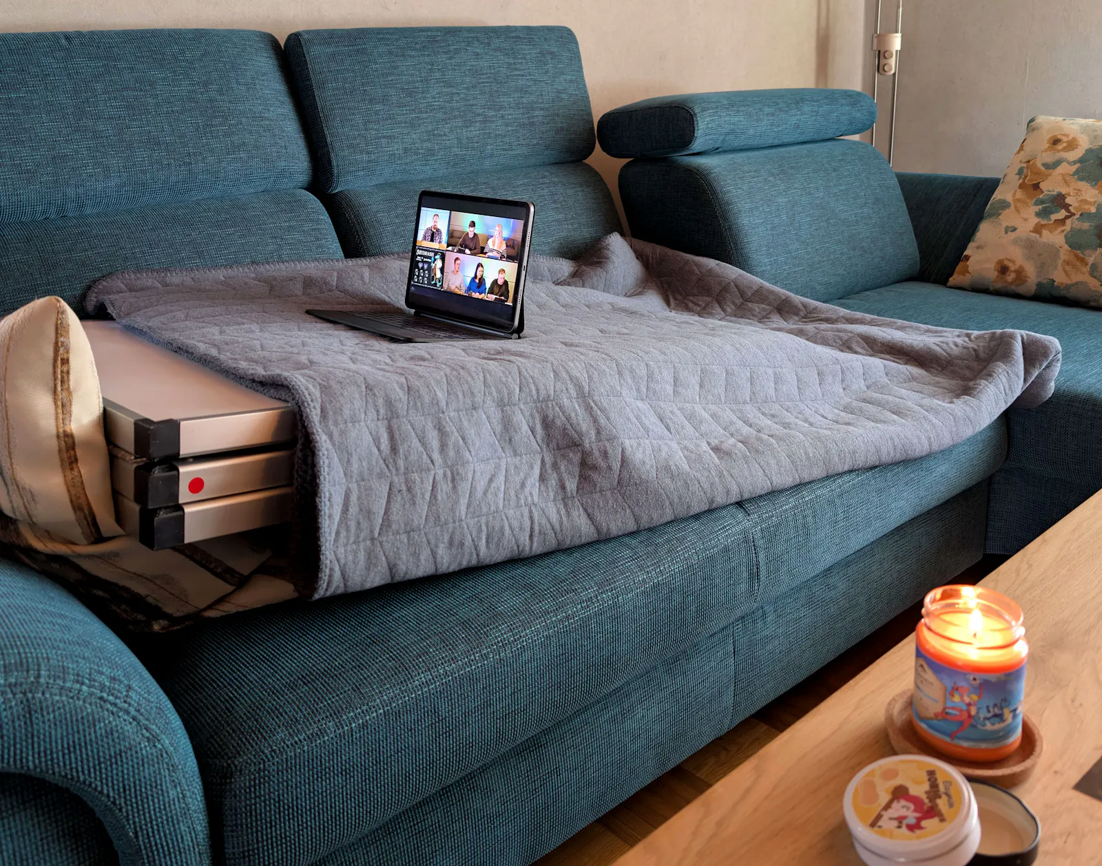 Der Tapeziertisch genießt das Leben in vollen Zügen: Er liegt auf dem Sofa, ist zugedeckt und schaut am Tablet die neueste Episode der Dice Actors. Nebenbei greift er bequem zum Tisch, um sich an Elaynies Honigbonbons zu bedienen und genießt den Duft sowie das Kerzenlicht der „Sommerpause“-Kerze.