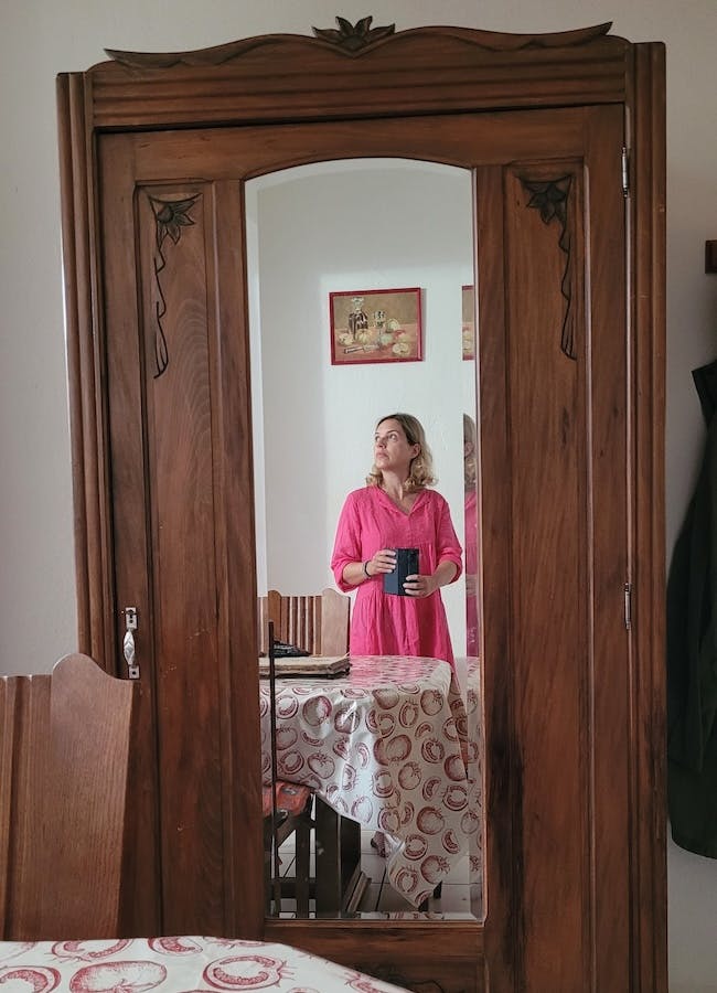 Christine Piontek im rosa Kleid fotografiert sich selbst im Spiegel eines alten Holzschranks.