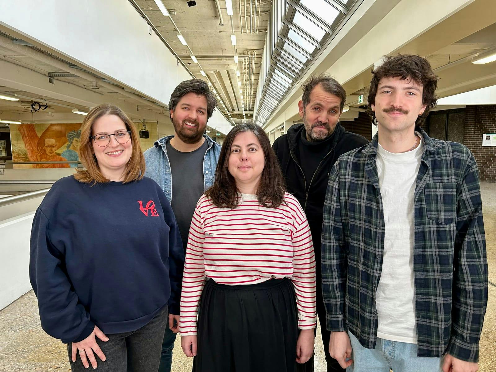 Fünf Personen in einem hellen, modernen Innenraum, lächelnd, Gruppenfoto